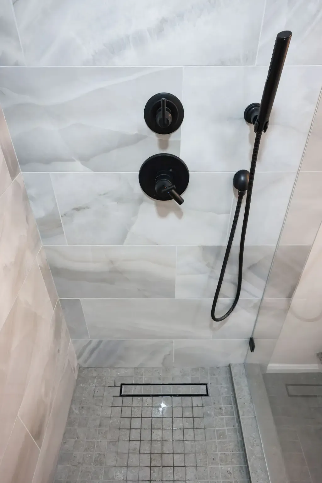 Marble shower stall with black fixtures, mosaic floor and slim drain