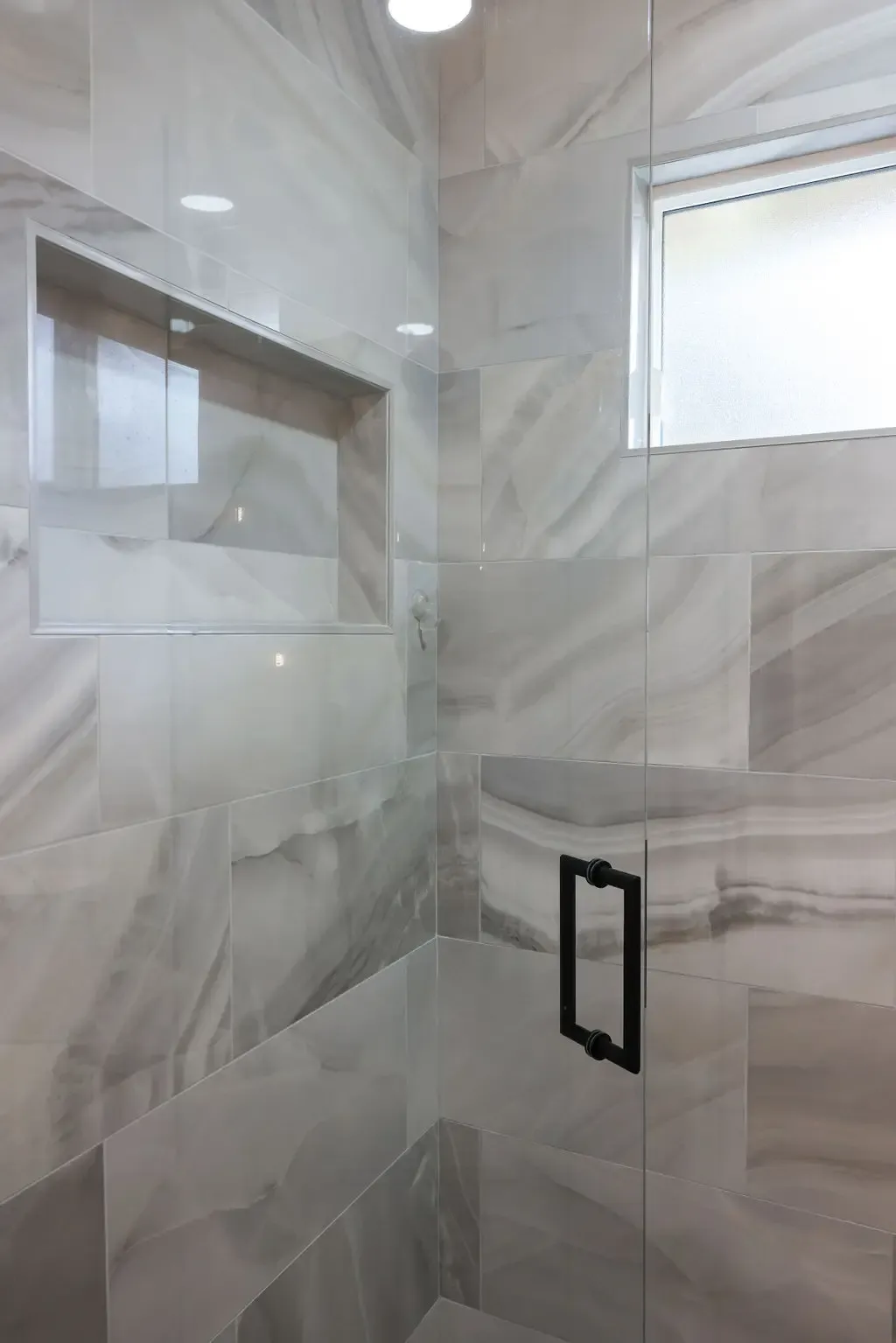 Marble-tiled shower wall with recessed niche and black glass-door handle