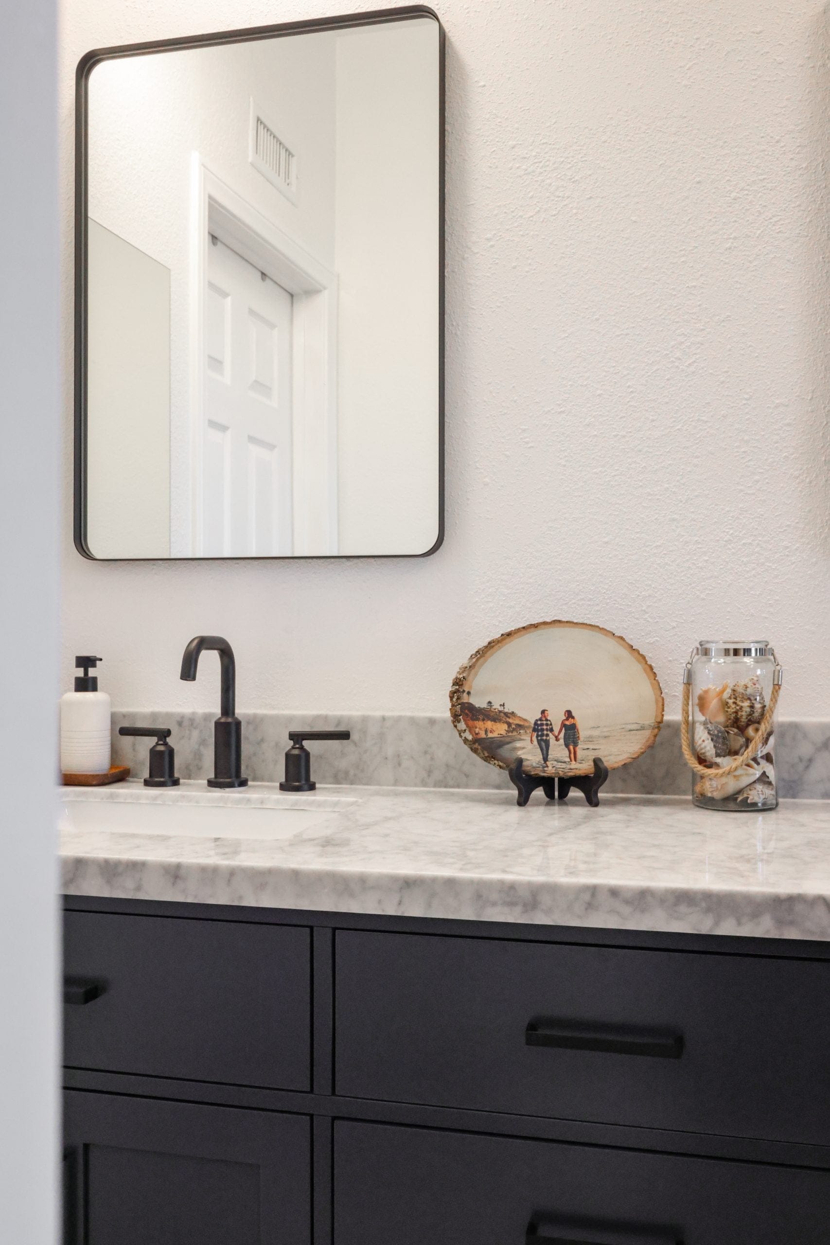 Marble-topped vanity with black faucet, framed mirror and coastal decor accents