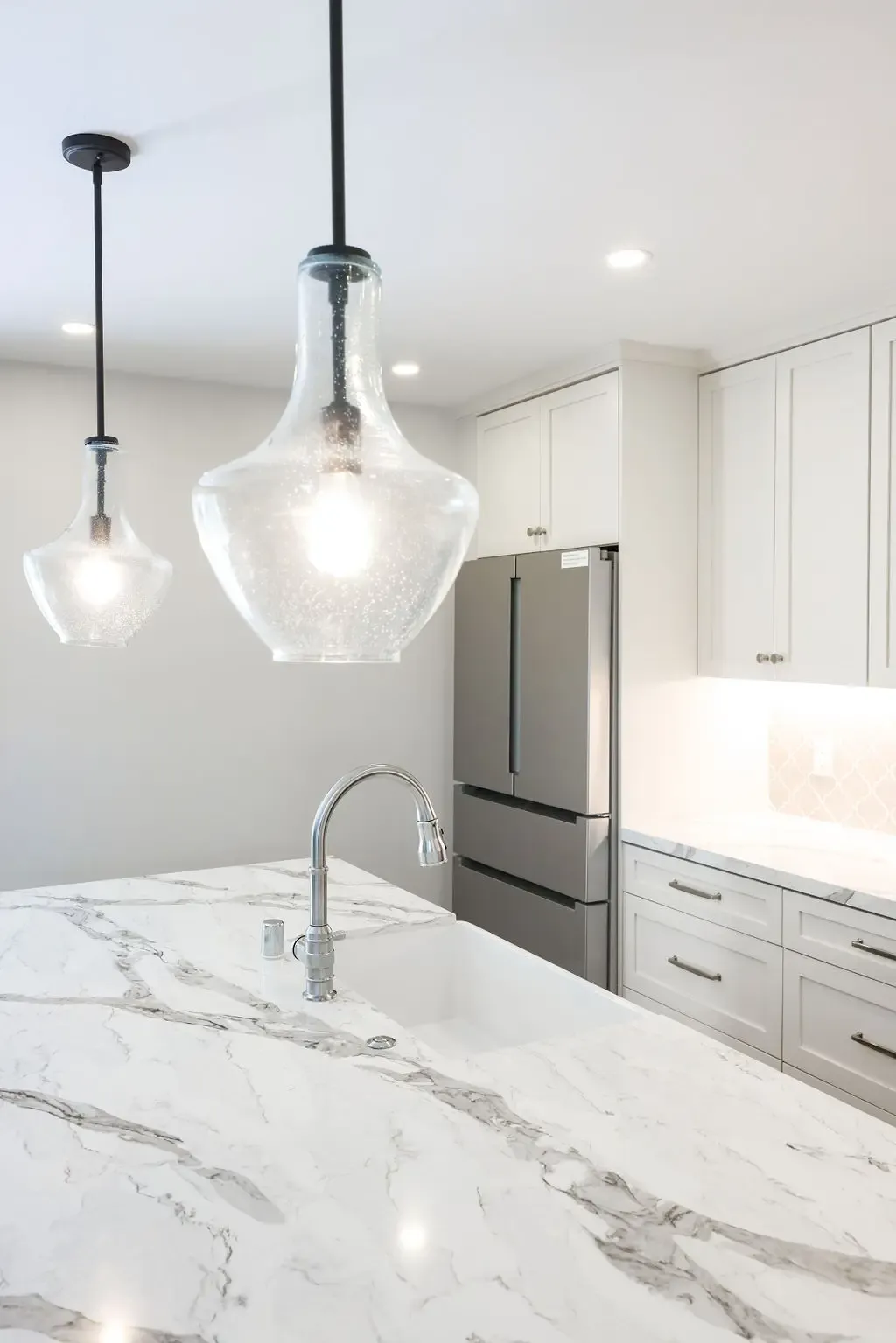 Marble waterfall island under seeded-glass pendant lights with bright white kitchen beyond