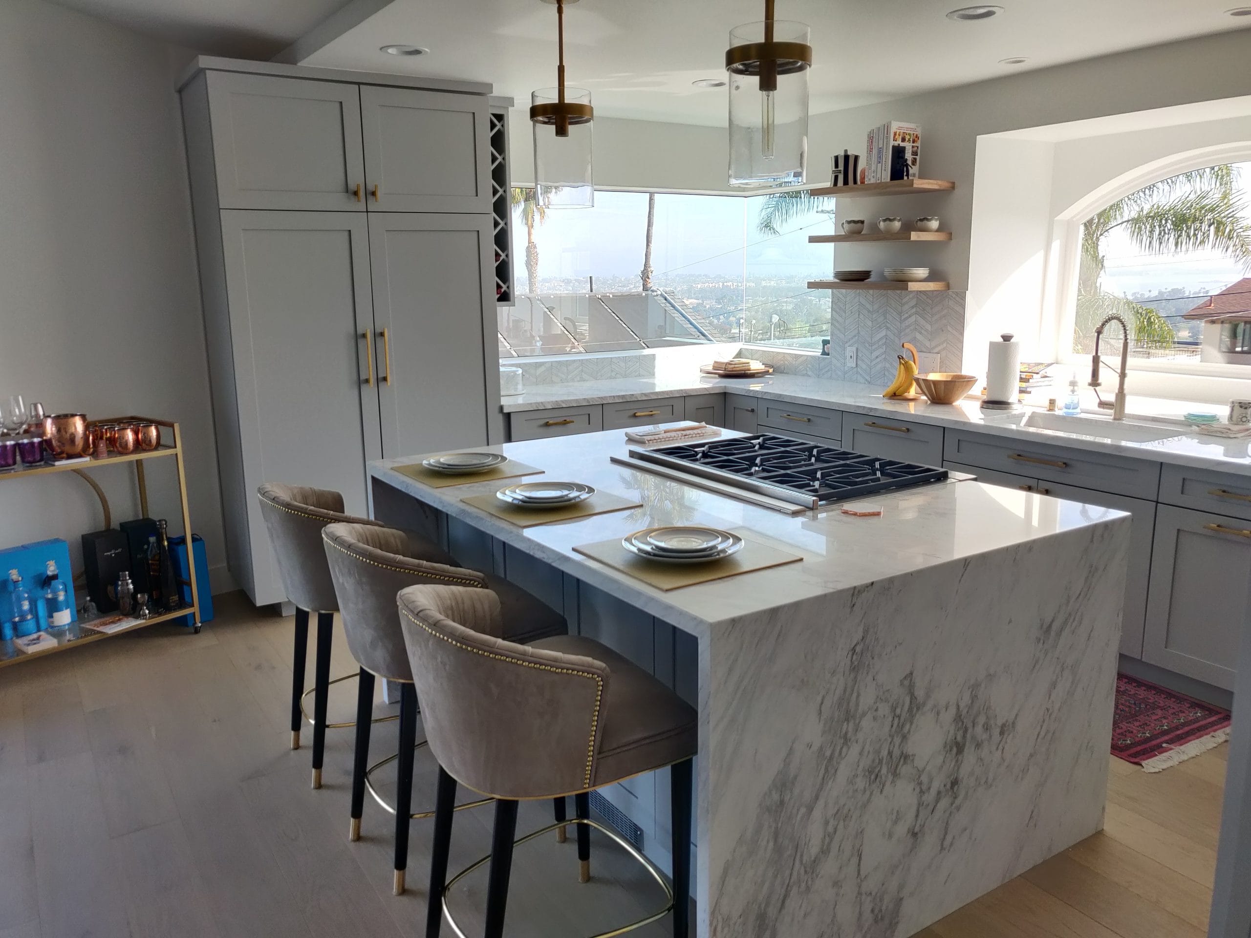 marble waterfall island with gas range, velvet stools, and gray shaker cabinetry