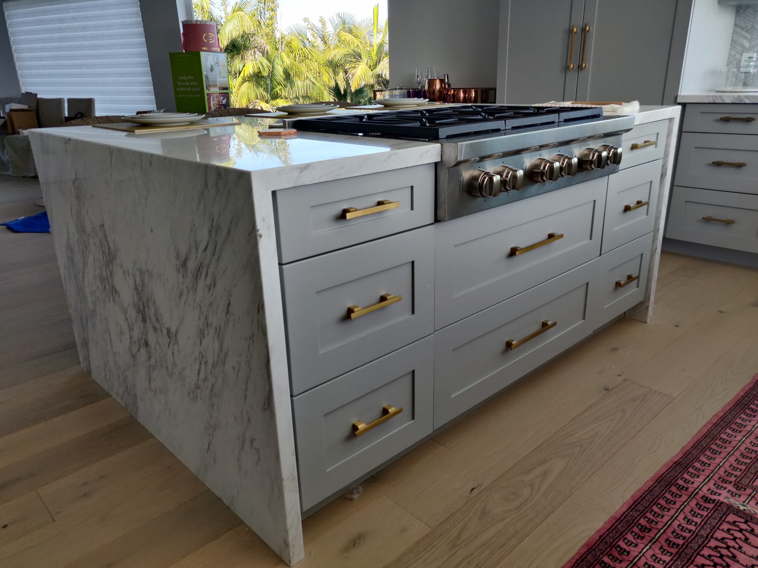 marble waterfall island with stainless gas rangetop and gold-handled gray drawers