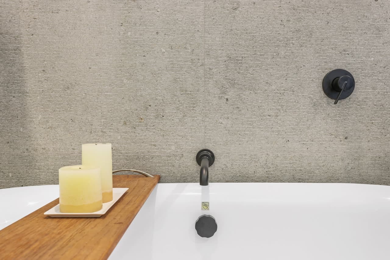 Matte black wall-mount tub filler against textured gray porcelain tile surround