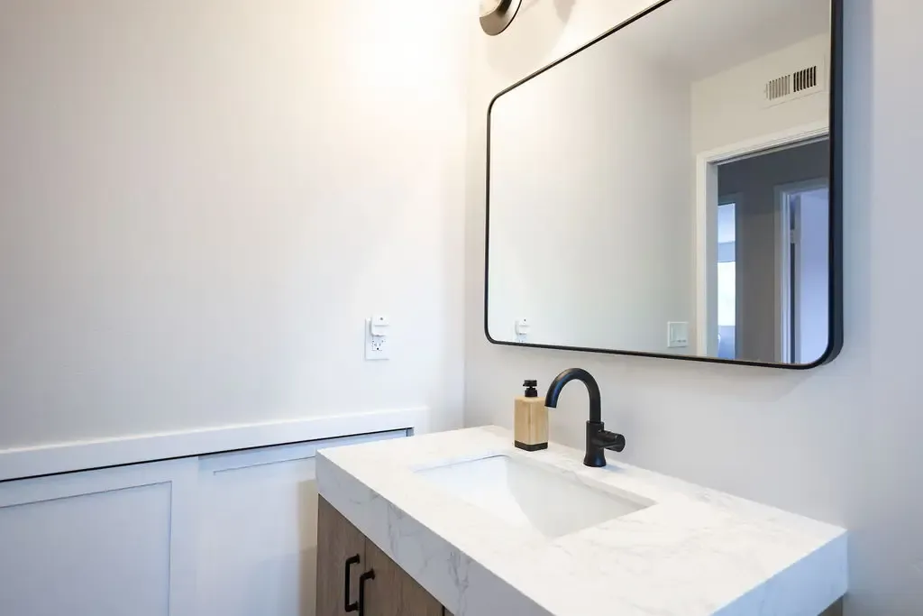 Minimalist powder room with marble-top wood vanity and rounded black-framed mirror