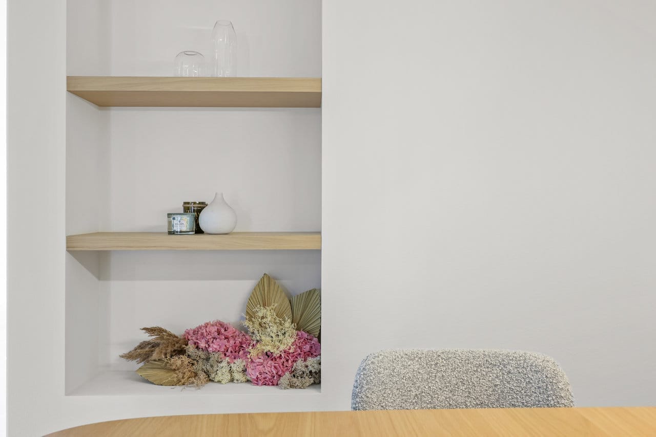 White recessed niche with light oak floating shelves and a dried floral arrangement