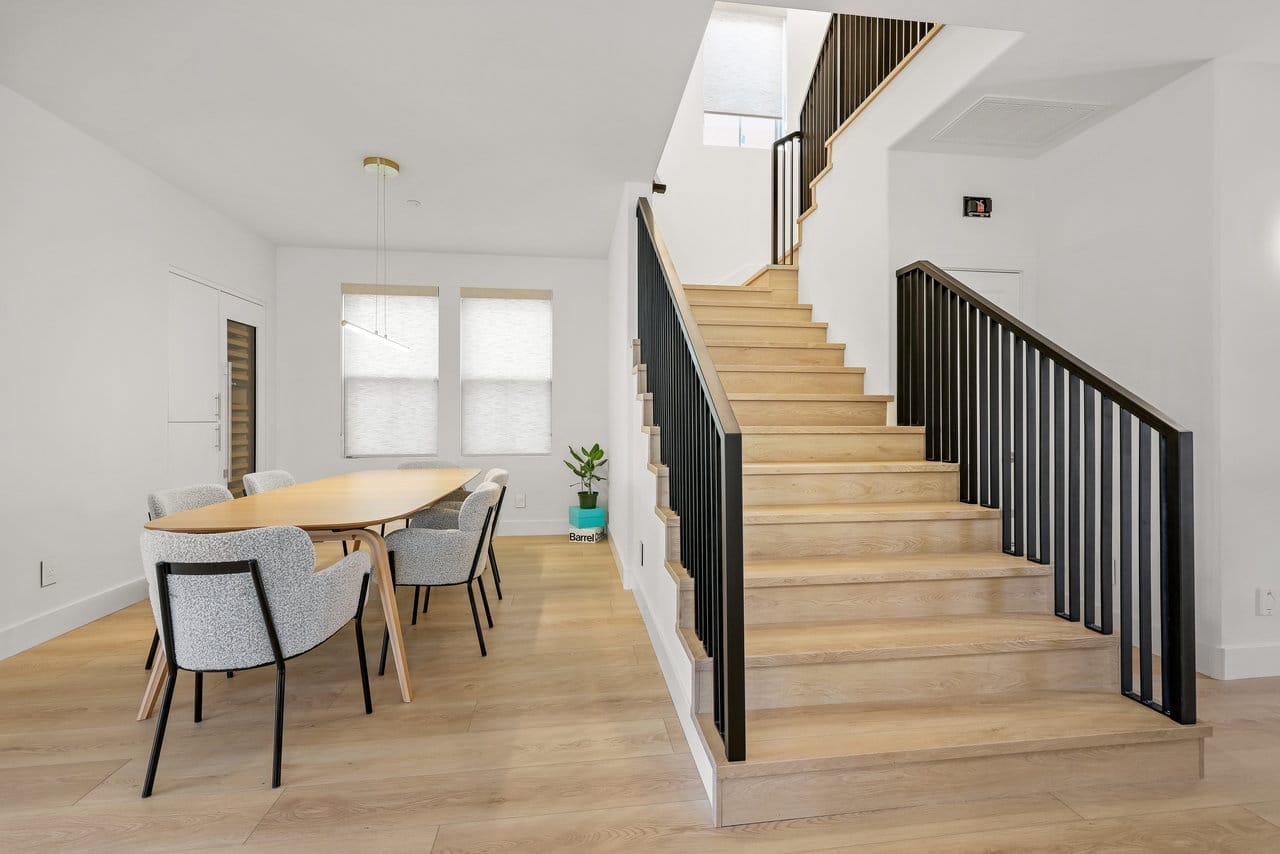 Open-concept dining area beside a light oak staircase with black metal railing and pale wood floors