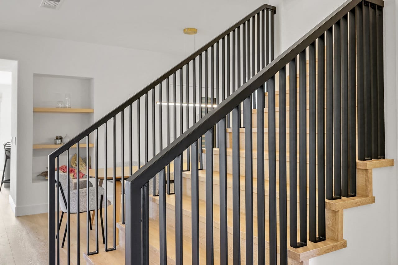 open staircase with black metal railing, light oak treads, and recessed display shelving
