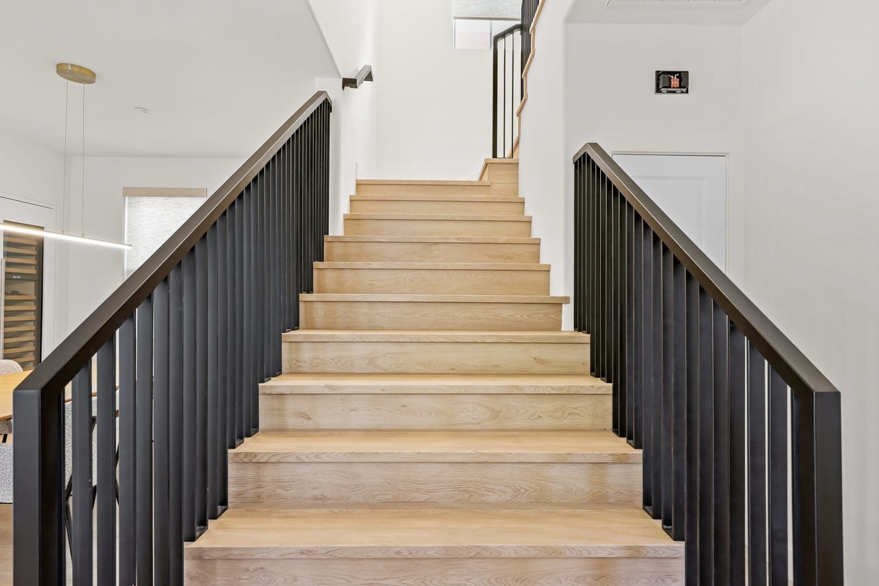 Wide oak staircase framed by black spindle railings in a bright white stairwell