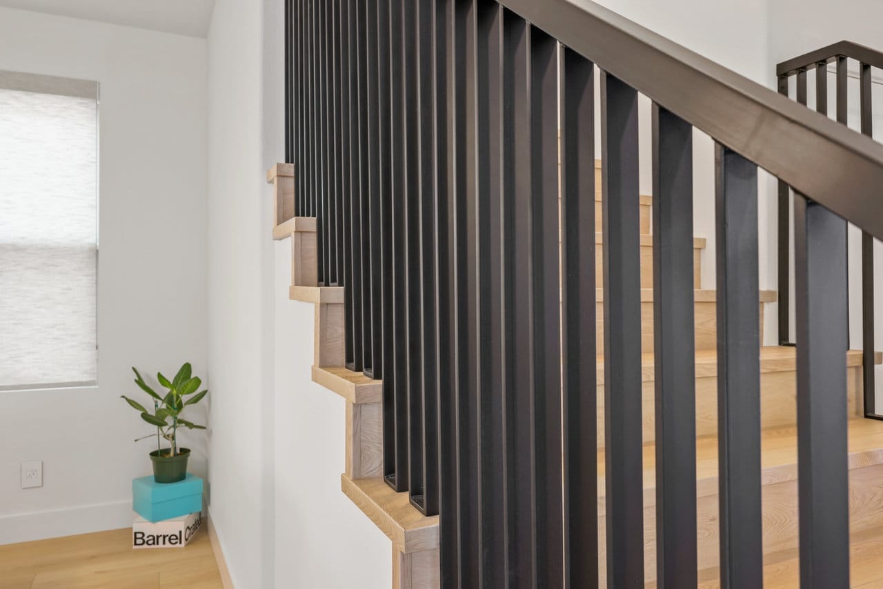 Modern staircase with vertical black metal railing, oak treads and white walls