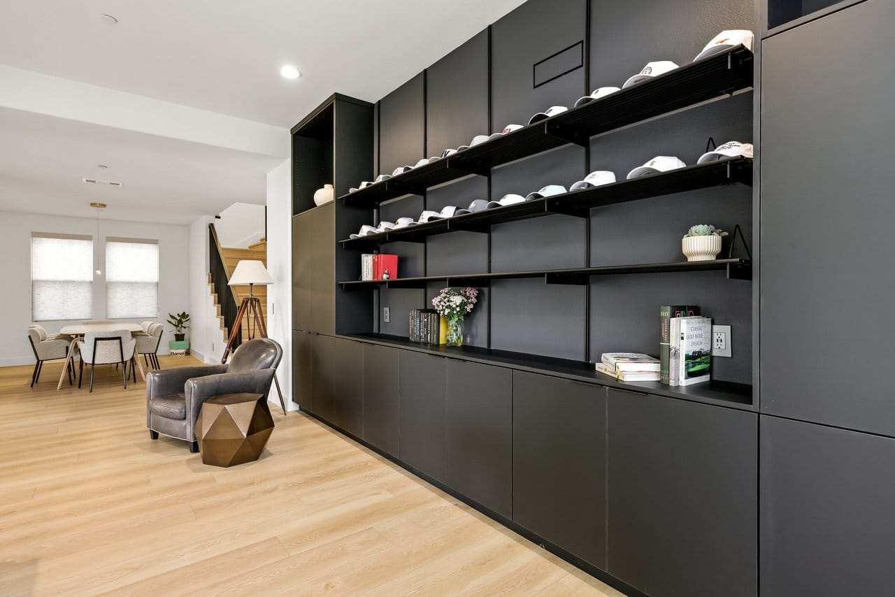 Modern black built-in shelving wall with cap display, leather chair, and oak flooring