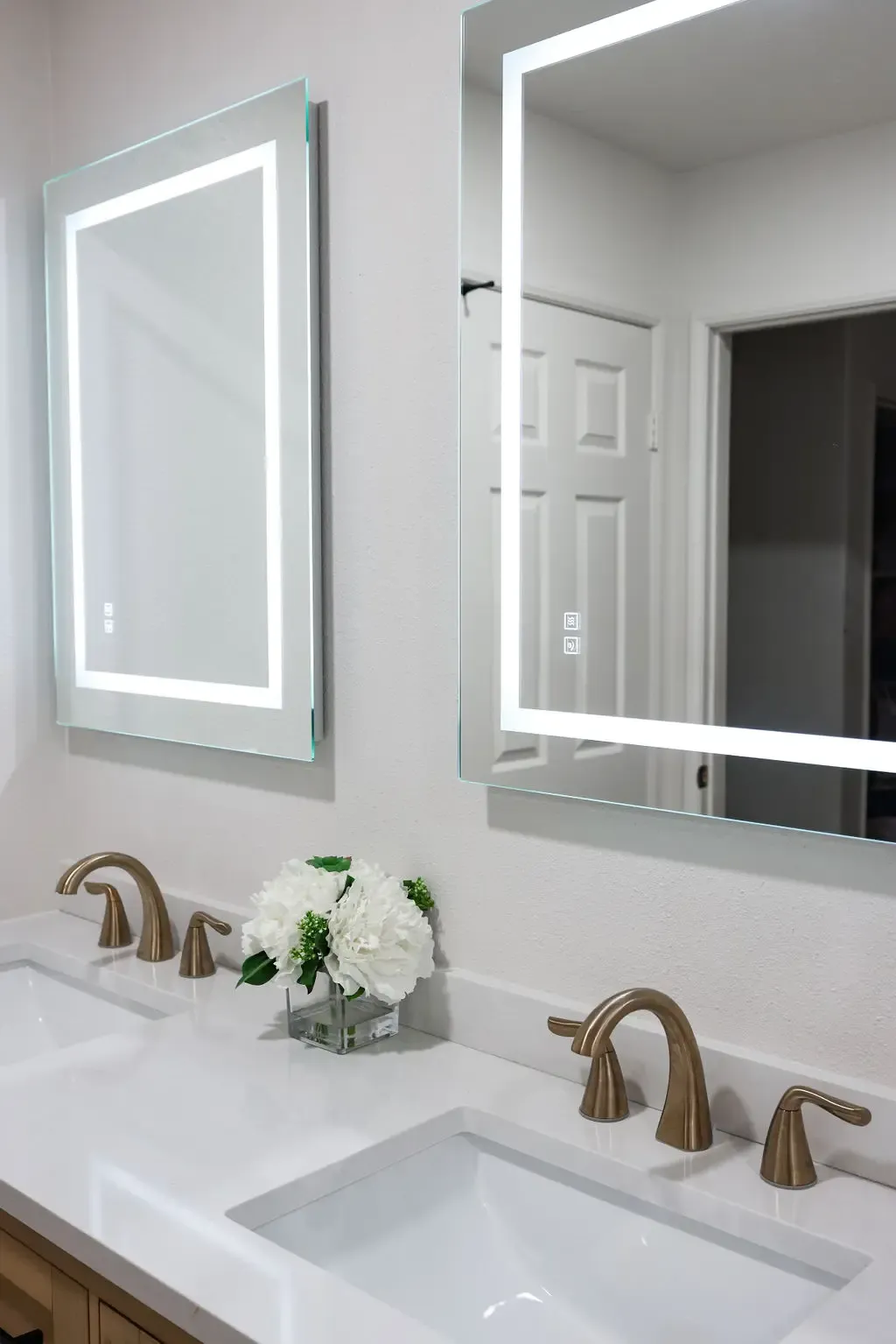 Modern bathroom vanity with two backlit mirrors, gold fixtures and fresh hydrangeas