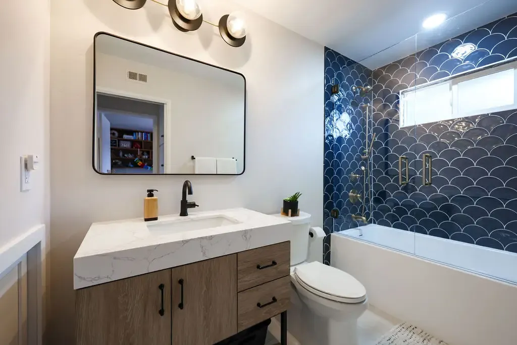 Modern bathroom with blue fish-scale tile tub surround and floating wood vanity