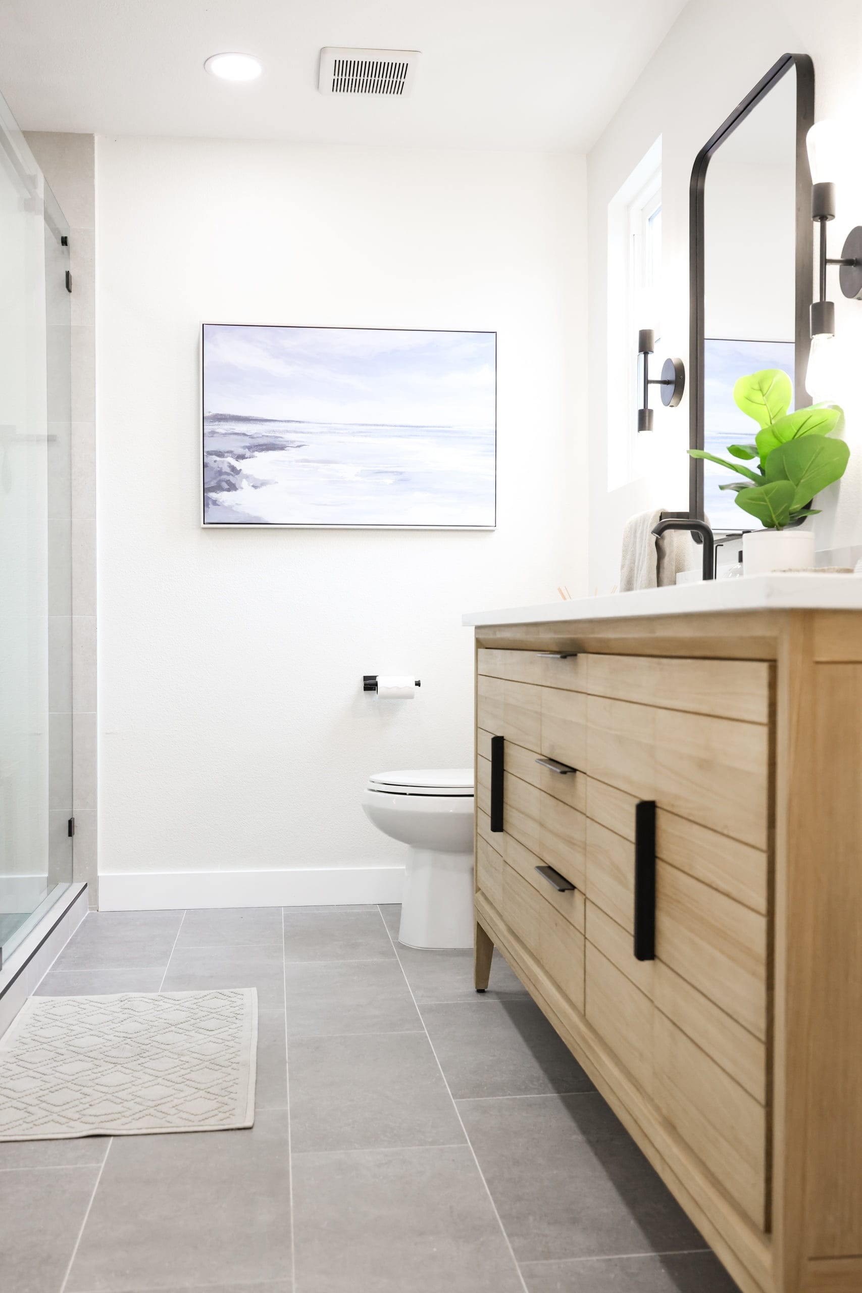 Modern bathroom with light wood vanity, gray tile floor and black hardware