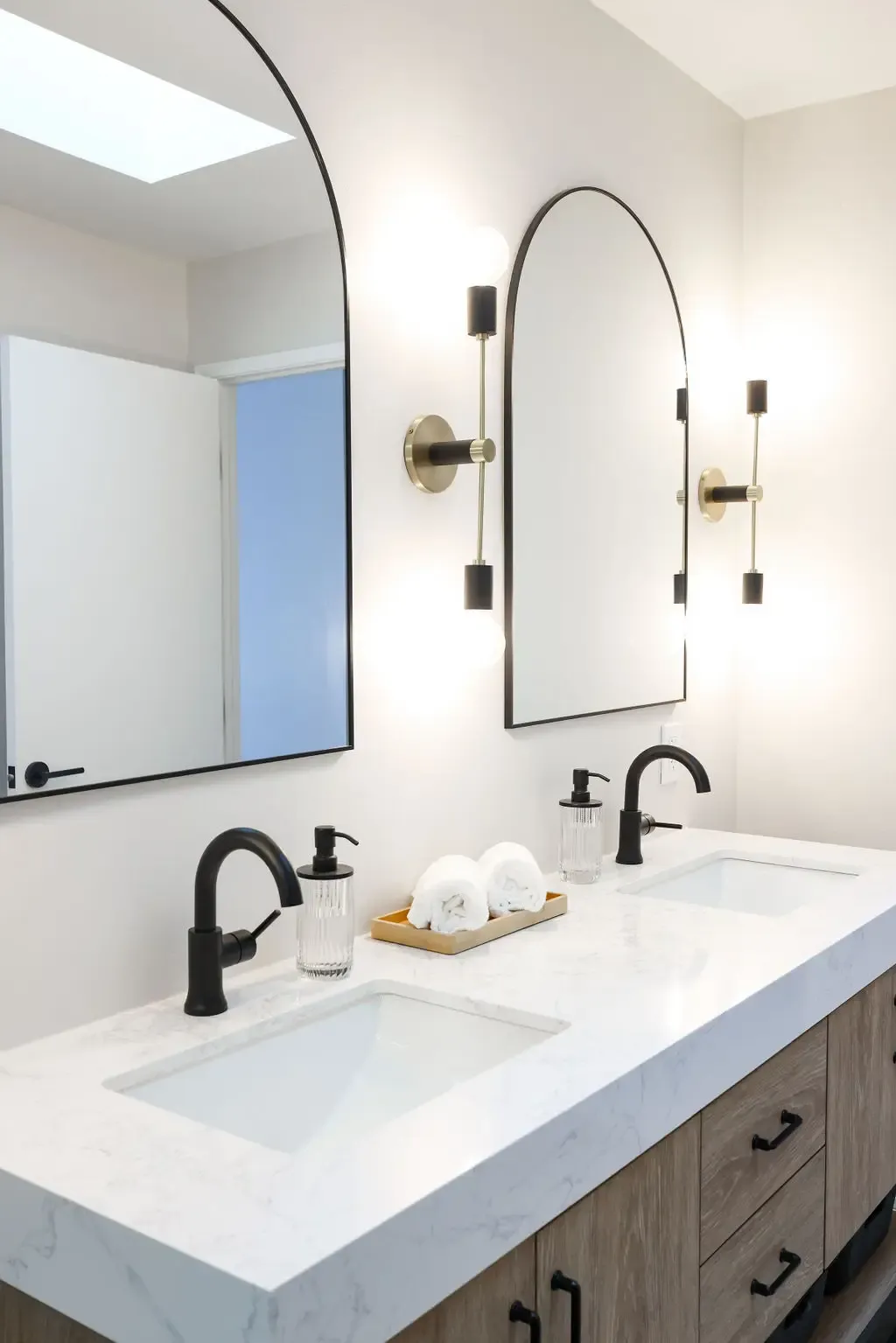 Modern double-vanity bathroom with arched mirrors, black faucets and quartz counter