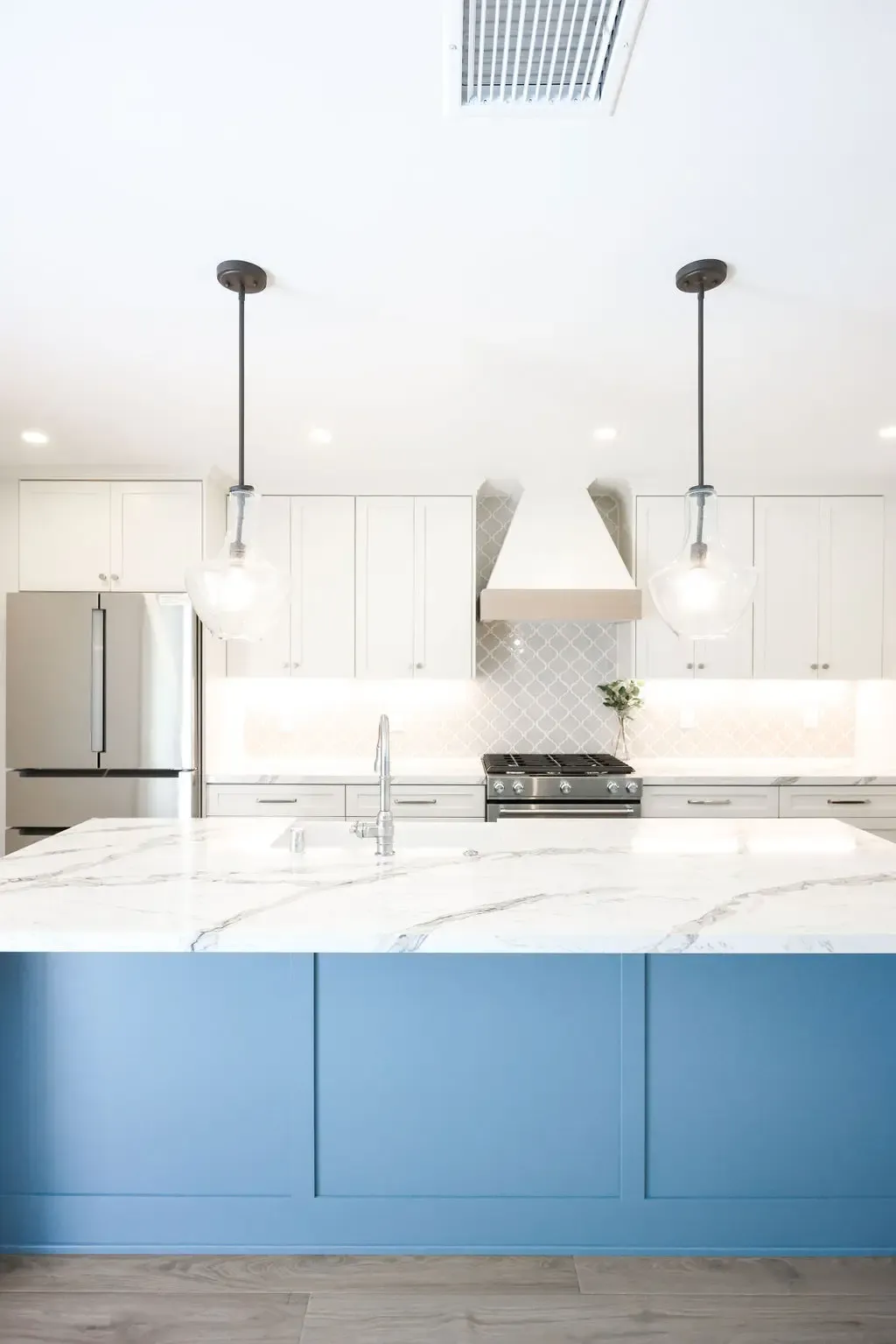 Modern kitchen island in blue cabinetry with veined marble waterfall countertop and glass pendants