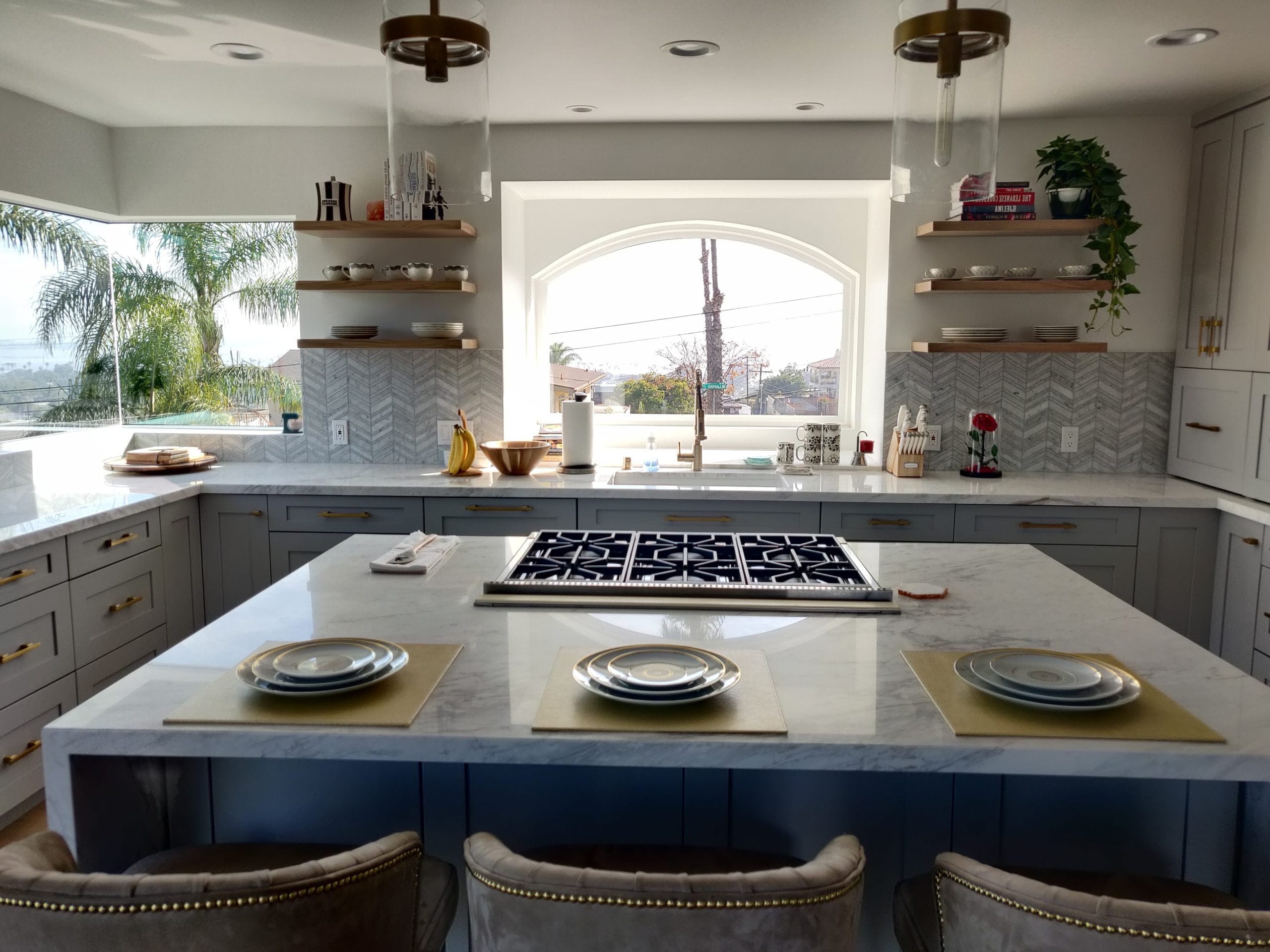 Modern kitchen island in marble with gray cabinets, gas range and arched window