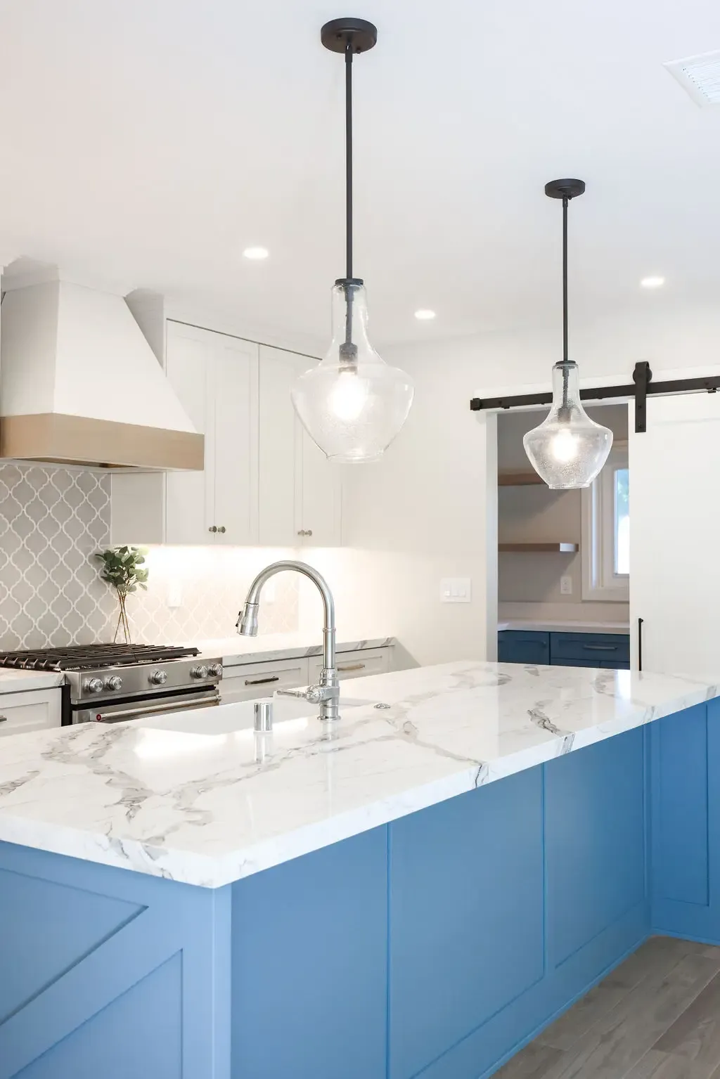 Modern kitchen with blue island, marble waterfall counter and glass pendant lights