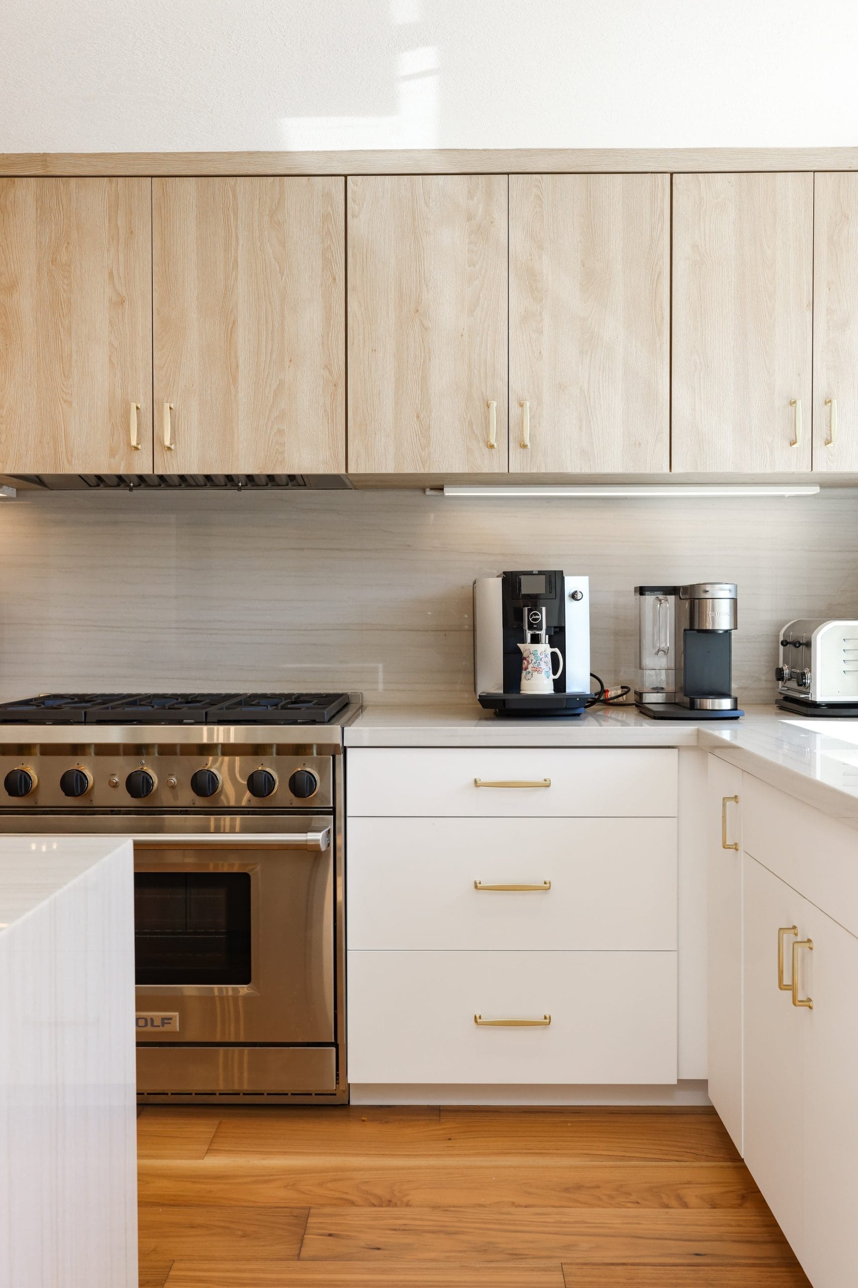 Modern kitchen with light oak cabinets, white quartz counters and stainless gas range