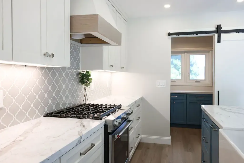 Modern kitchen with white shaker cabinets, wood vent hood, and gray scalloped tile backsplash