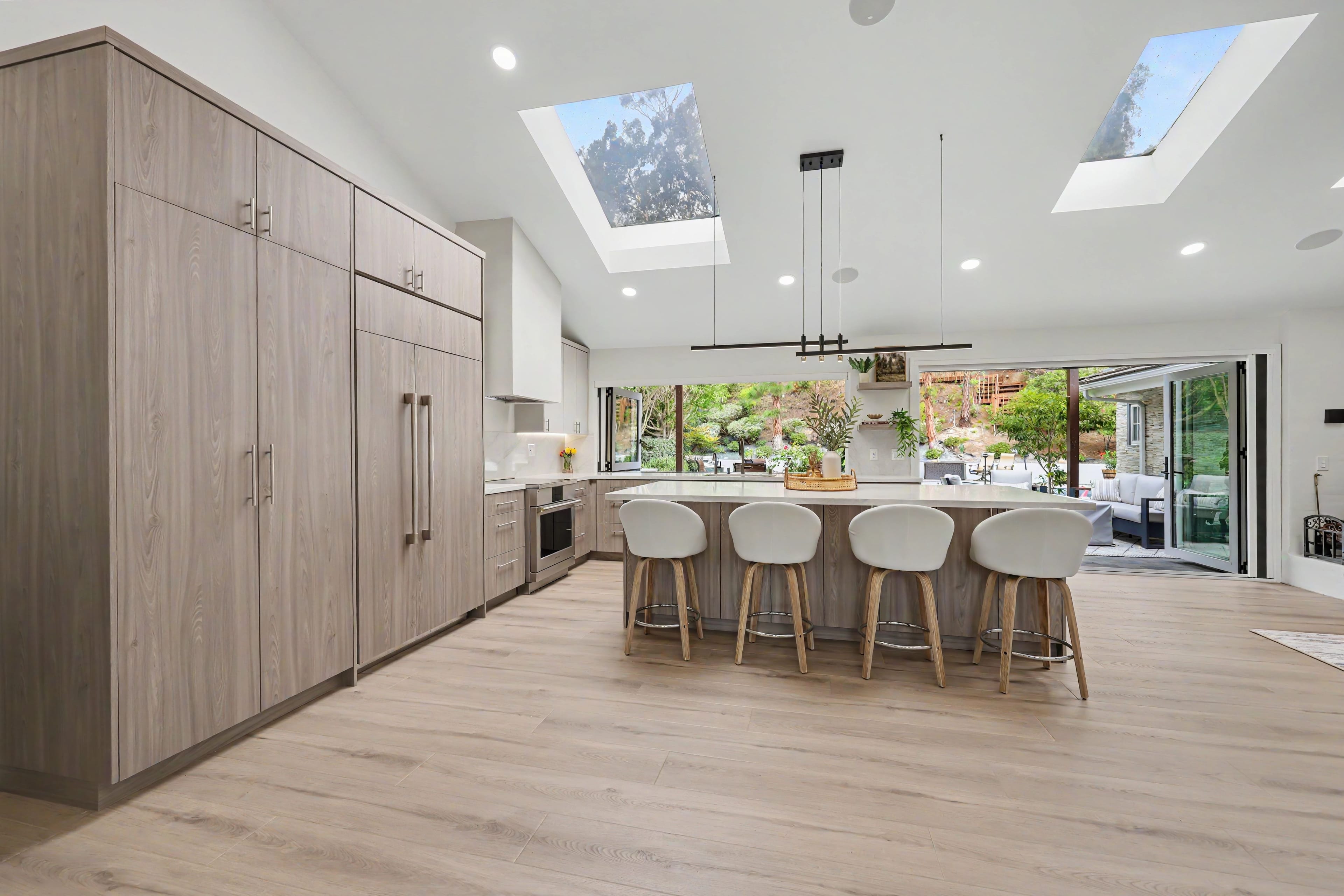 Spacious modern kitchen with floor-to-ceiling wood-grain cabinets, a large center island, vaulted ceilings with skylights, and wide open doors leading to the backyard.