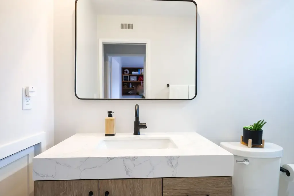 Modern powder room with floating wood vanity, marble-look quartz top and black framed mirror