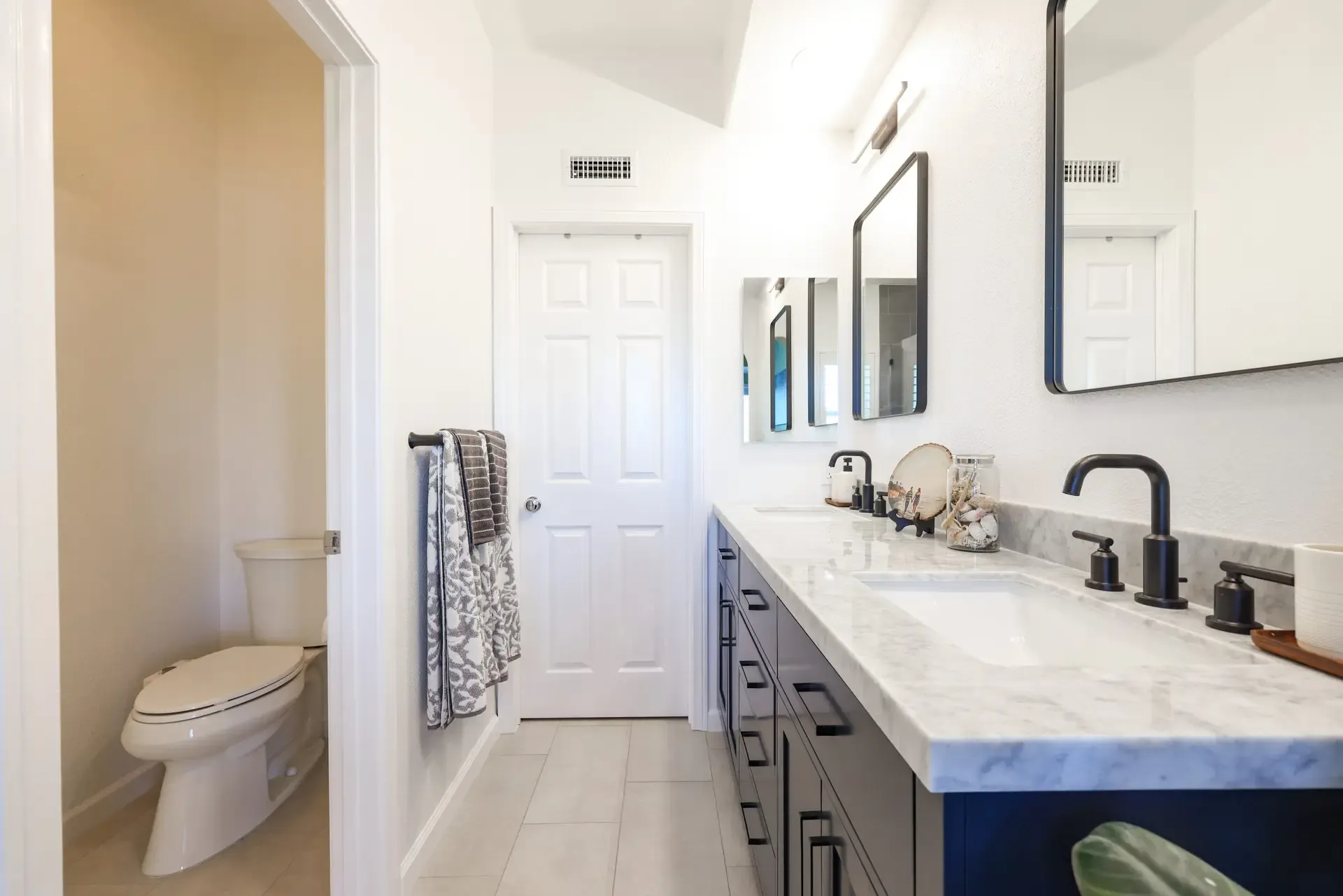 Narrow bathroom with navy double vanity, marble counter, and black fixtures