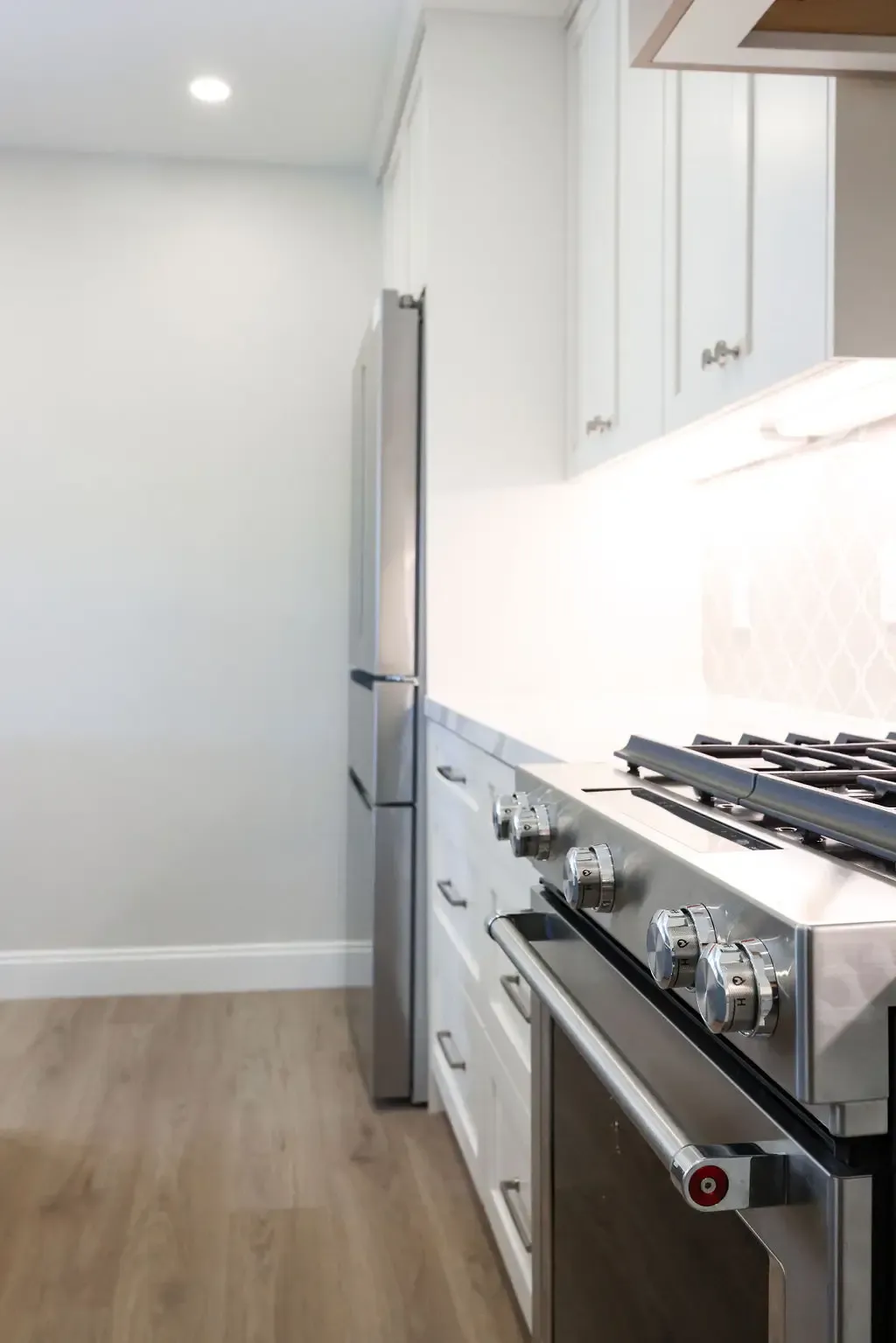 Narrow modern kitchen with stainless range, white cabinets, and light wood flooring