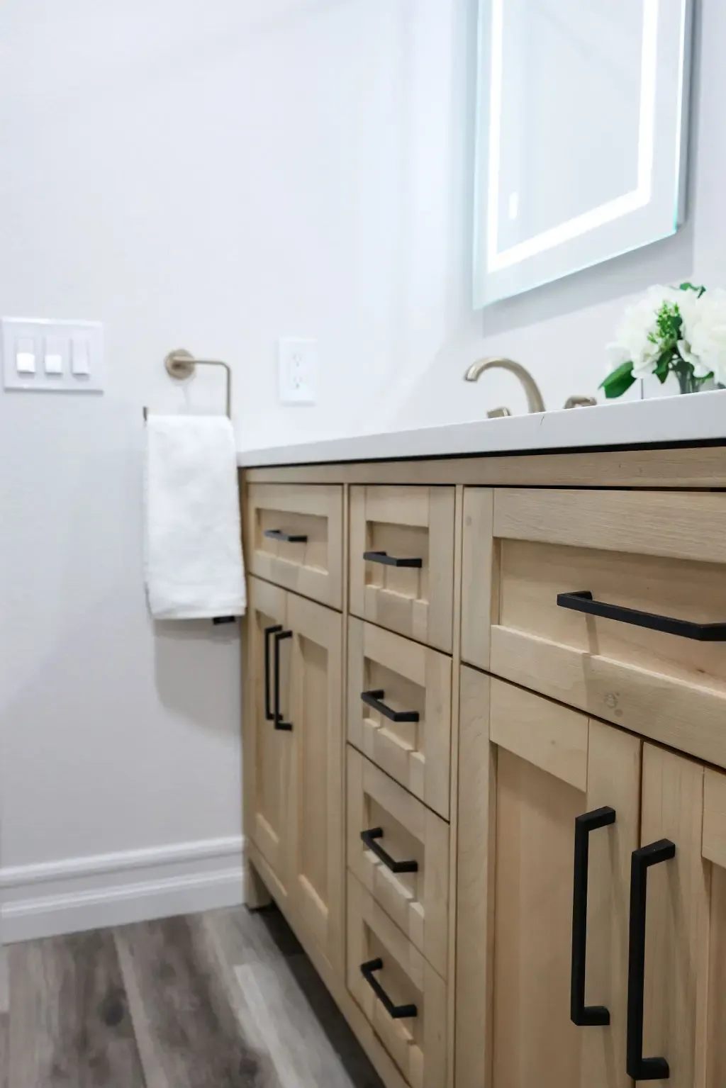 Natural wood bathroom vanity with black hardware, gray top and lit mirror