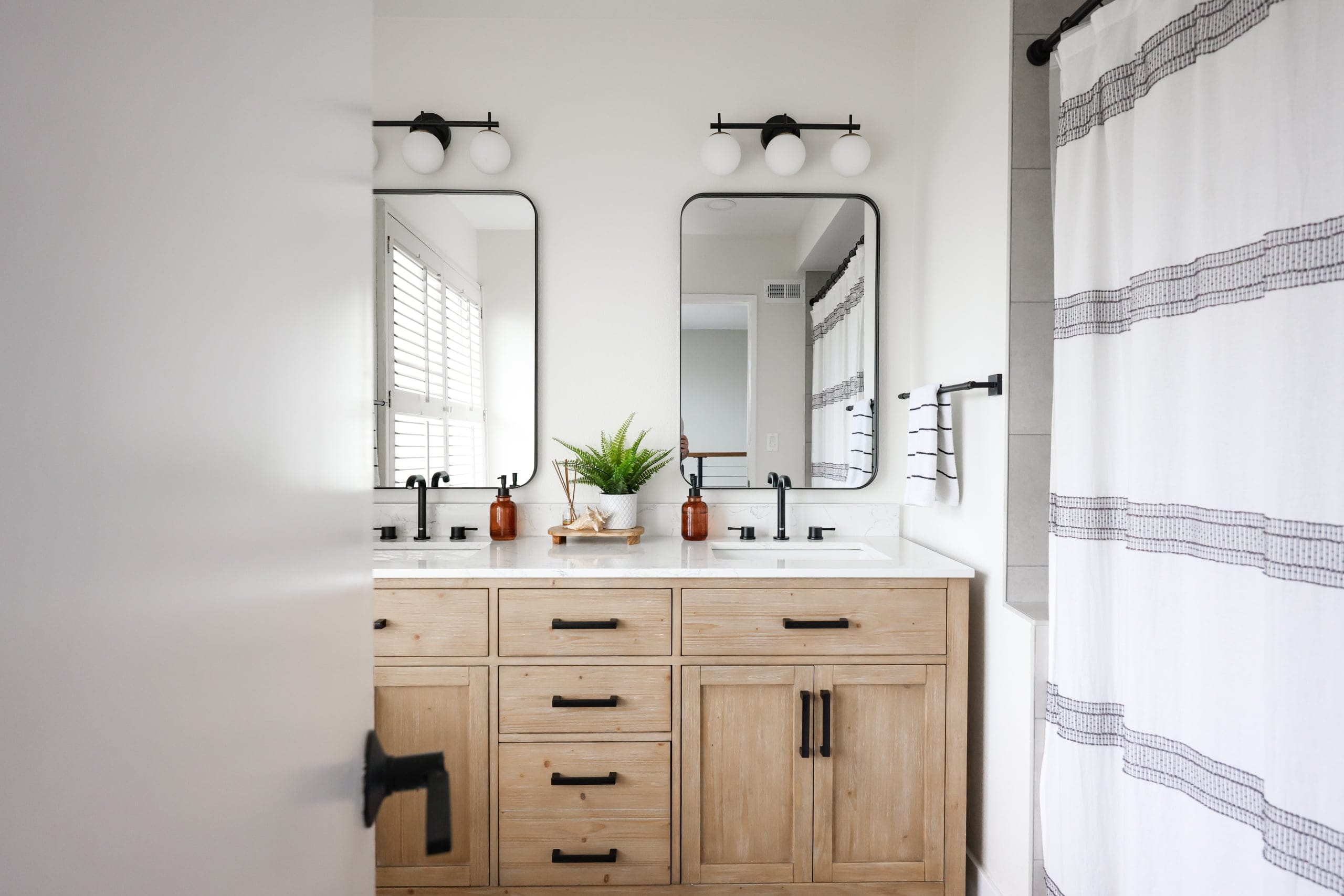 Natural-wood double vanity with black hardware and twin arched mirrors