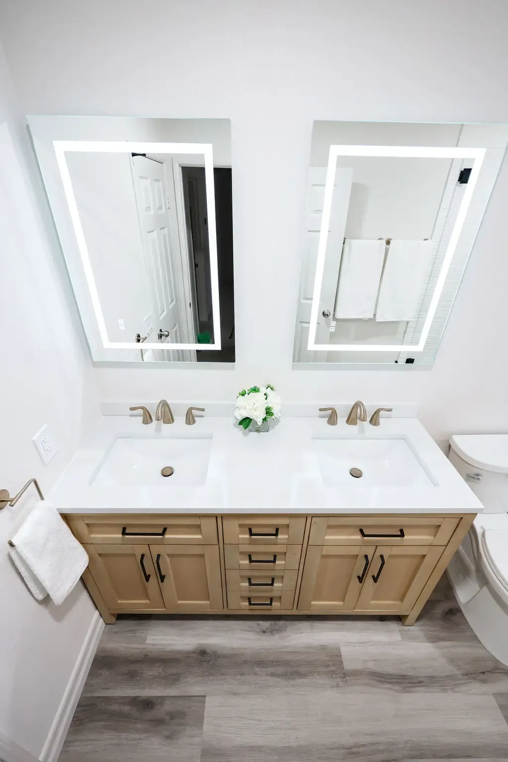 natural wood double vanity with white counters and LED backlit mirrors over wood-look floor