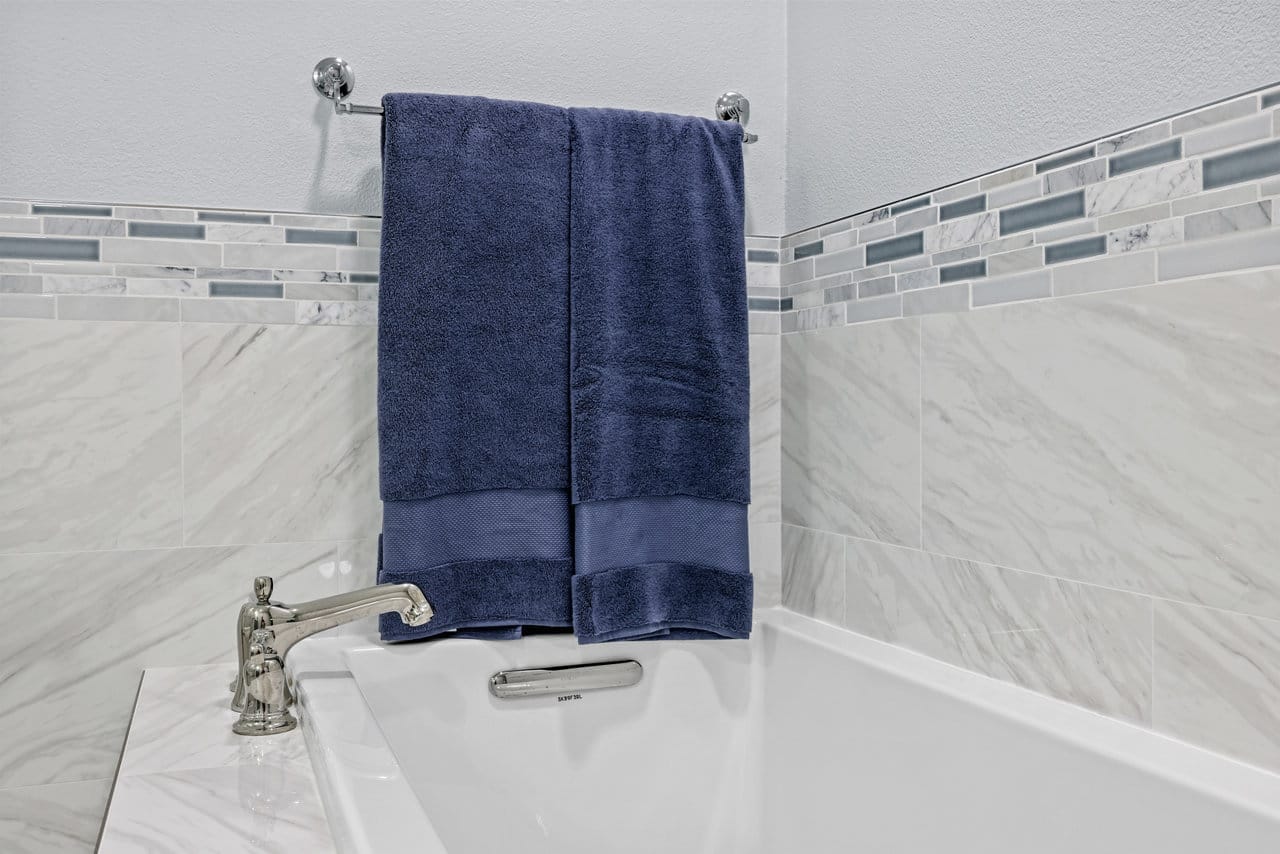 navy bath towel on chrome bar above white tub with marble-look tile surround