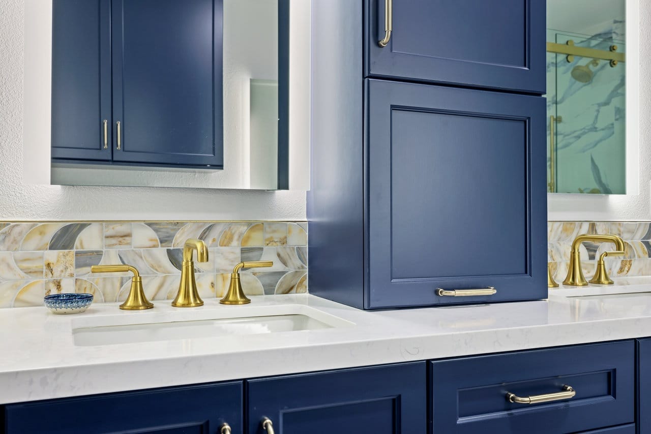 navy double vanity detail with brass widespread faucets and iridescent glass mosaic backsplash