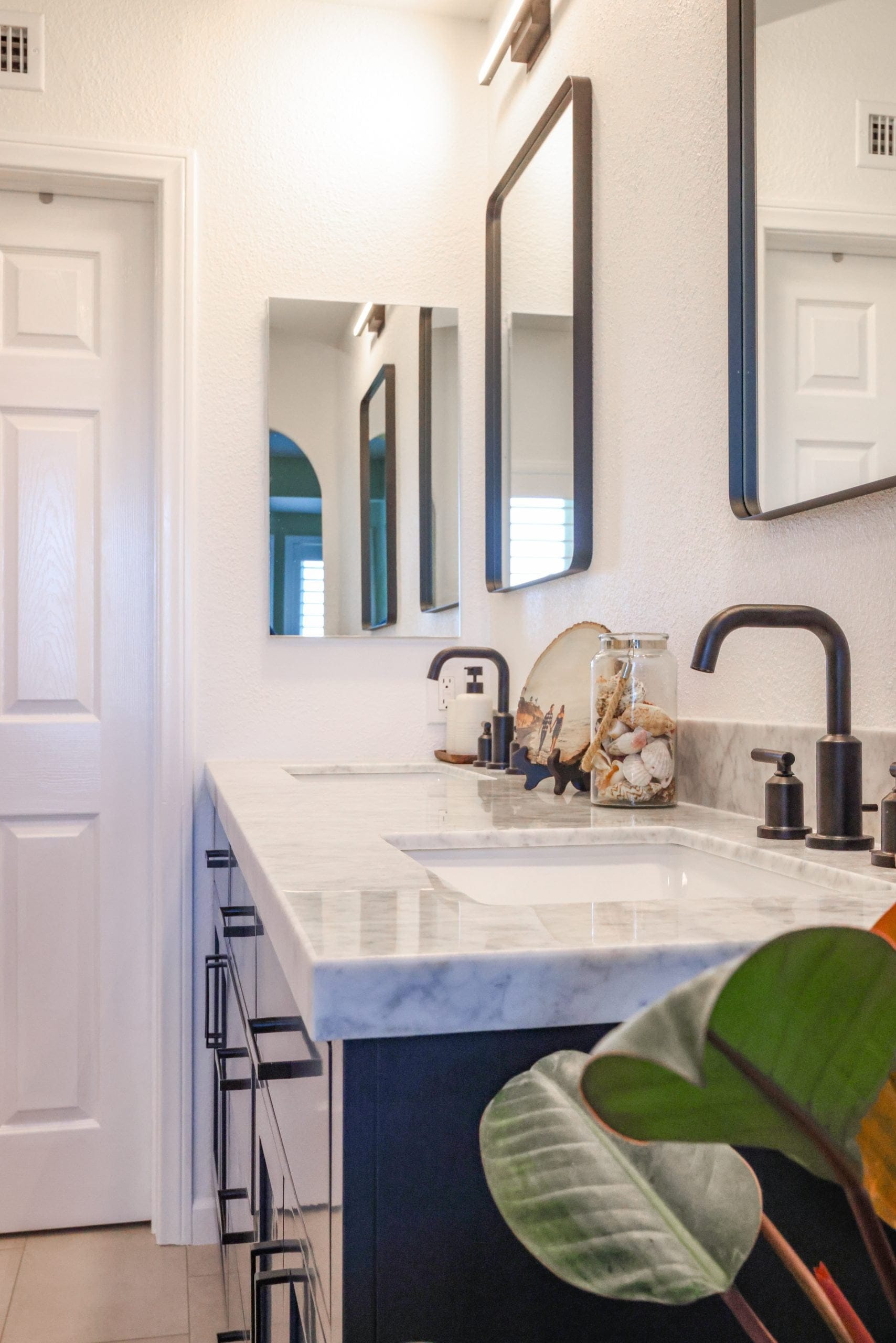 navy vanity bathroom with marble counter, black framed mirrors and matte black fixtures