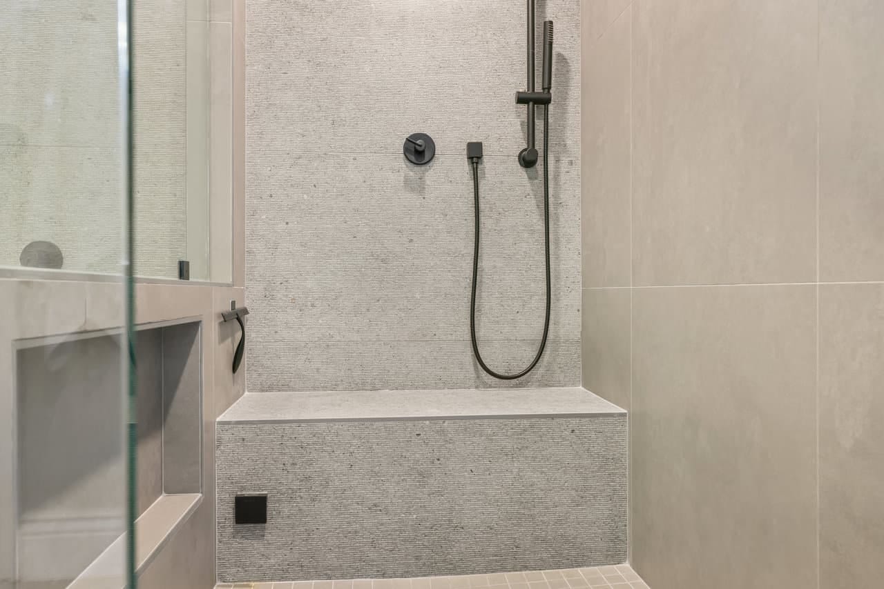 neutral gray shower with built-in bench and black handheld rail fixture