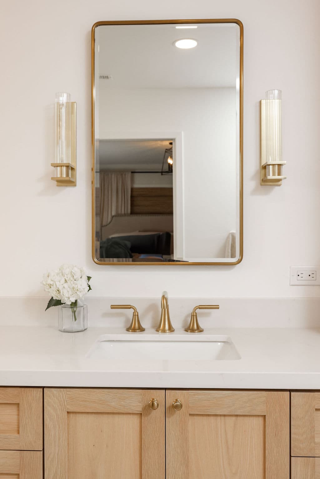 oak vanity with white quartz top, brass faucet and gold-framed mirror between sconces