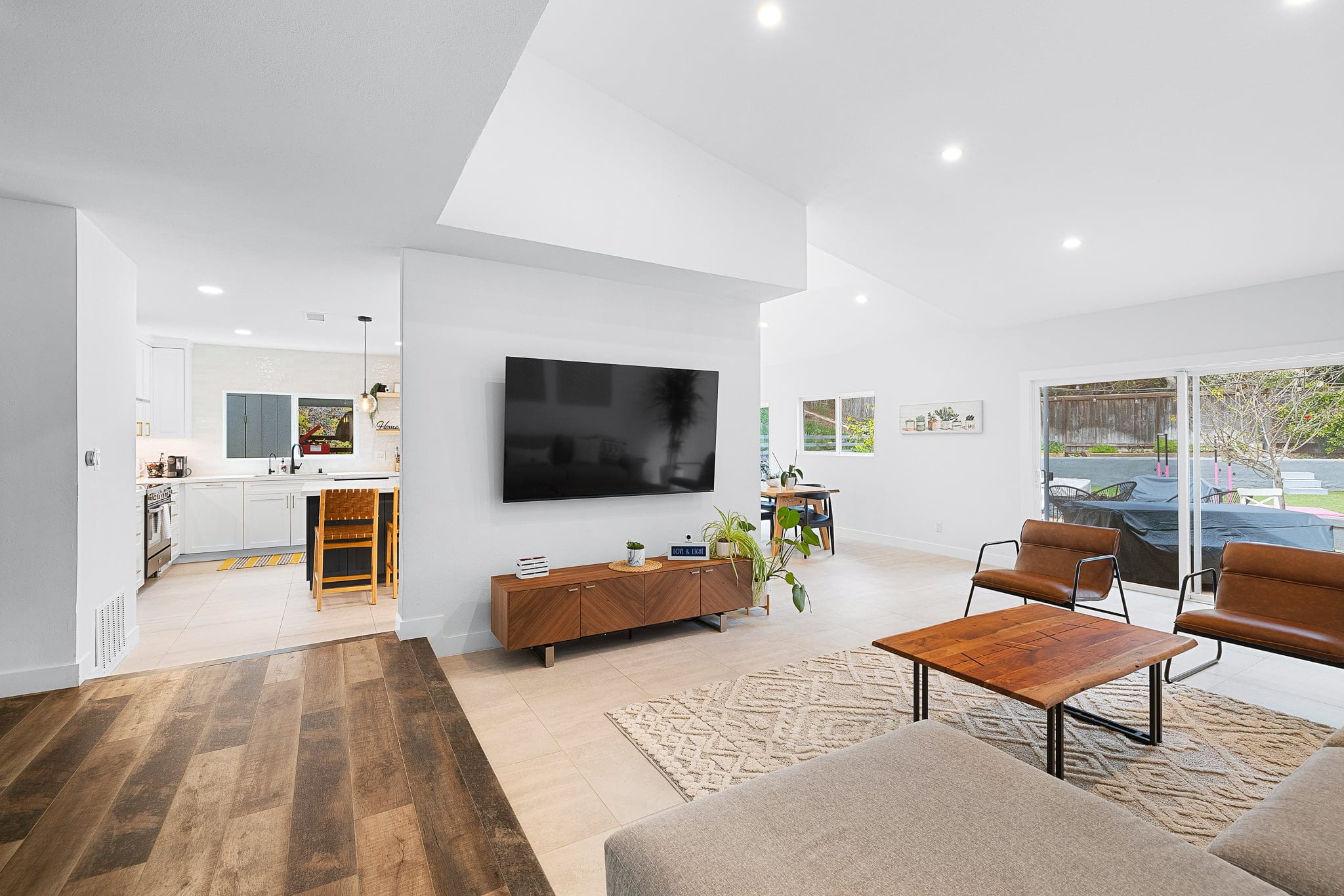 Open-concept great room with mounted TV opening to a white kitchen beyond