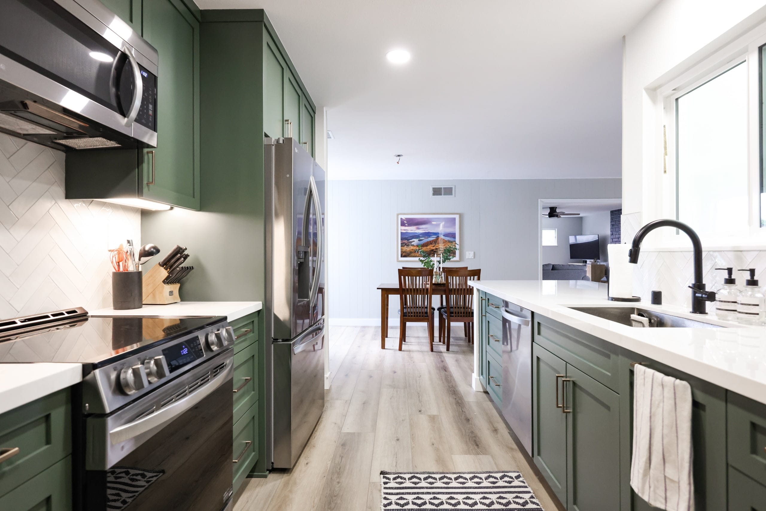 Open green kitchen with stainless range, farmhouse sink and adjoining dining nook