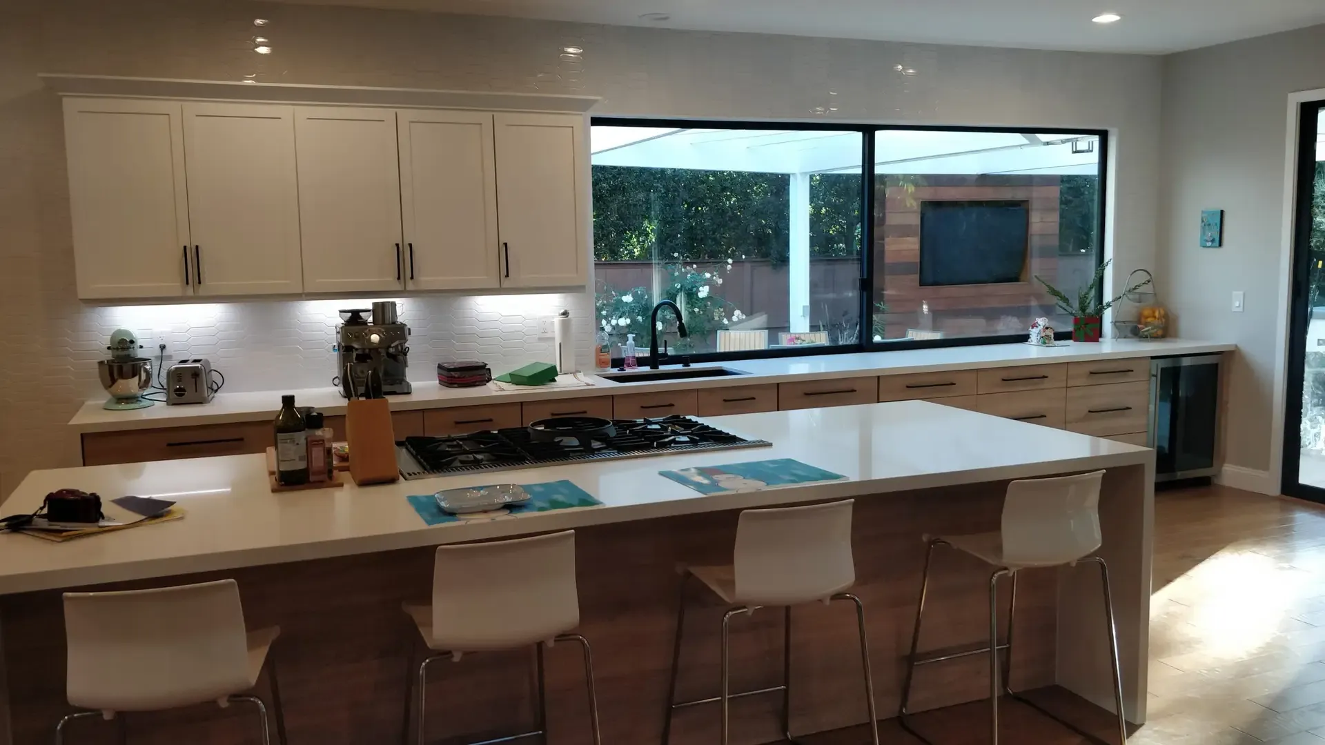 Open kitchen featuring waterfall quartz island, white shaker uppers and bar seating