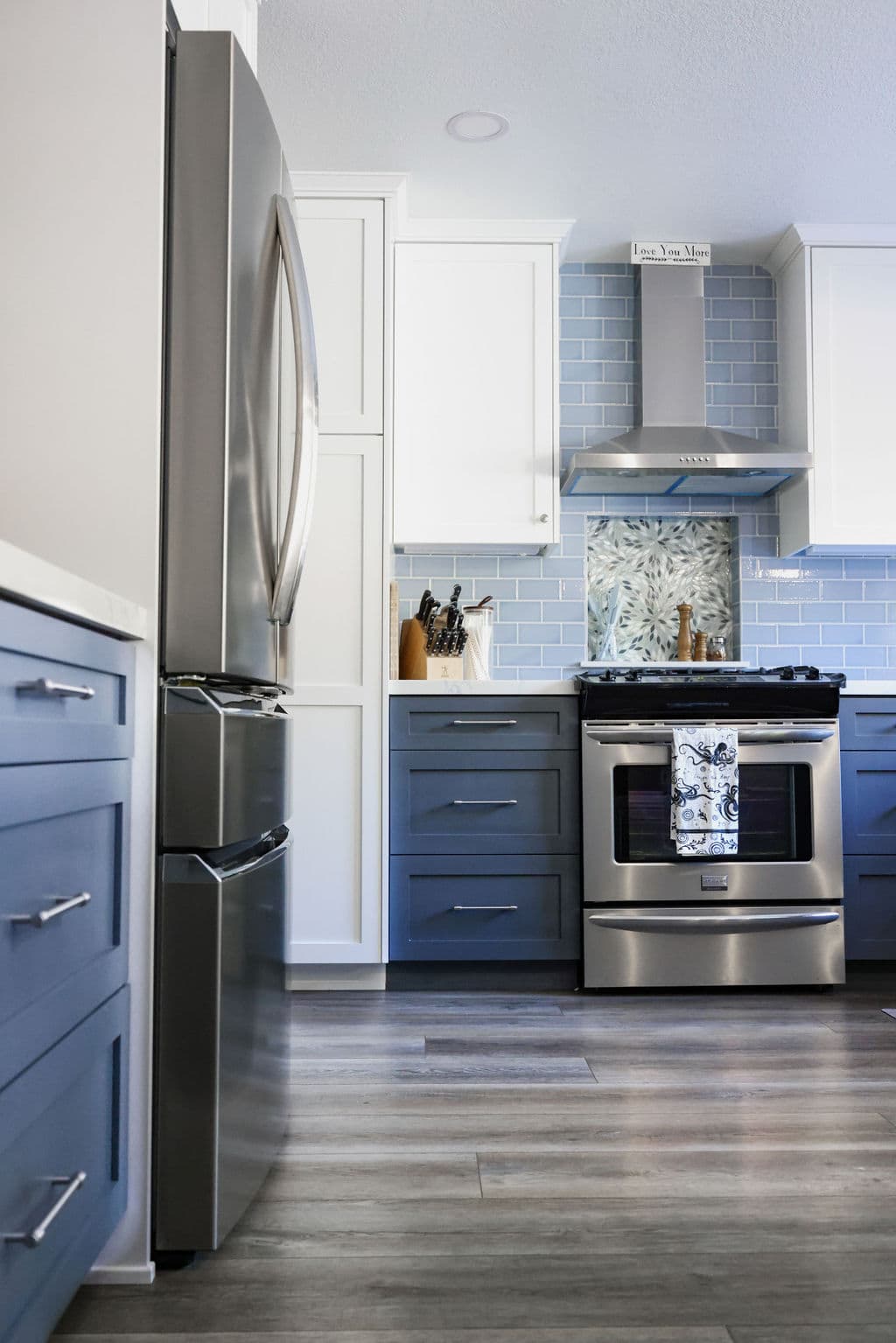 Open kitchen view with navy cabinetry, stainless refrigerator and blue tile backsplash on wood floors