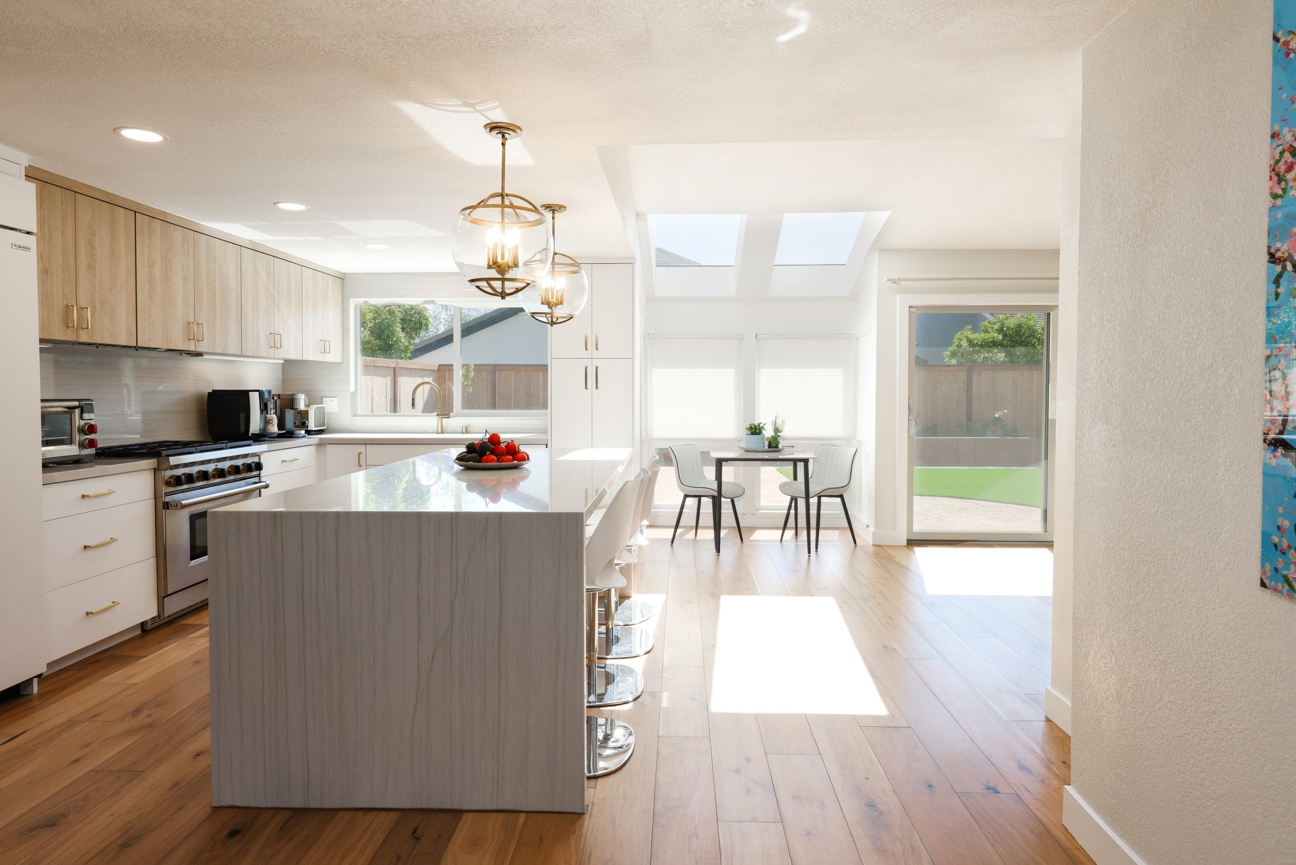 Open kitchen with light oak cabinets, quartz waterfall island and hardwood floors
