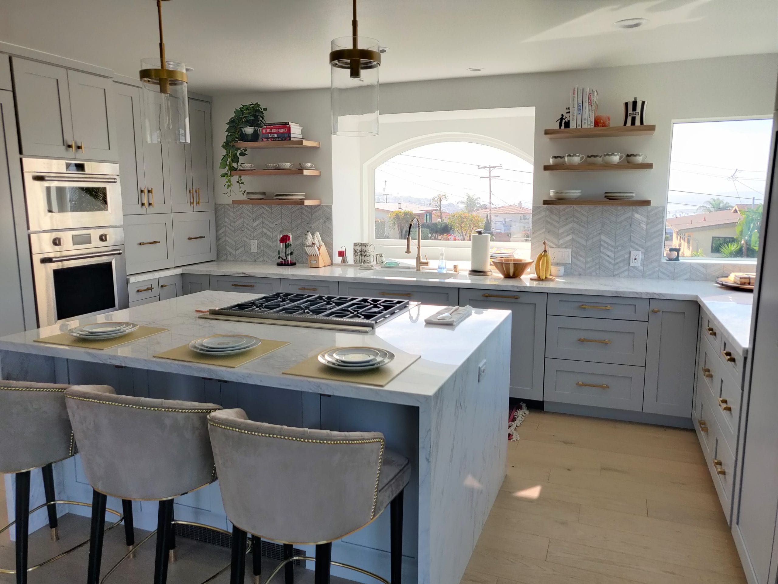 Open kitchen with marble waterfall island, gray cabinetry, gas cooktop and velvet barstools
