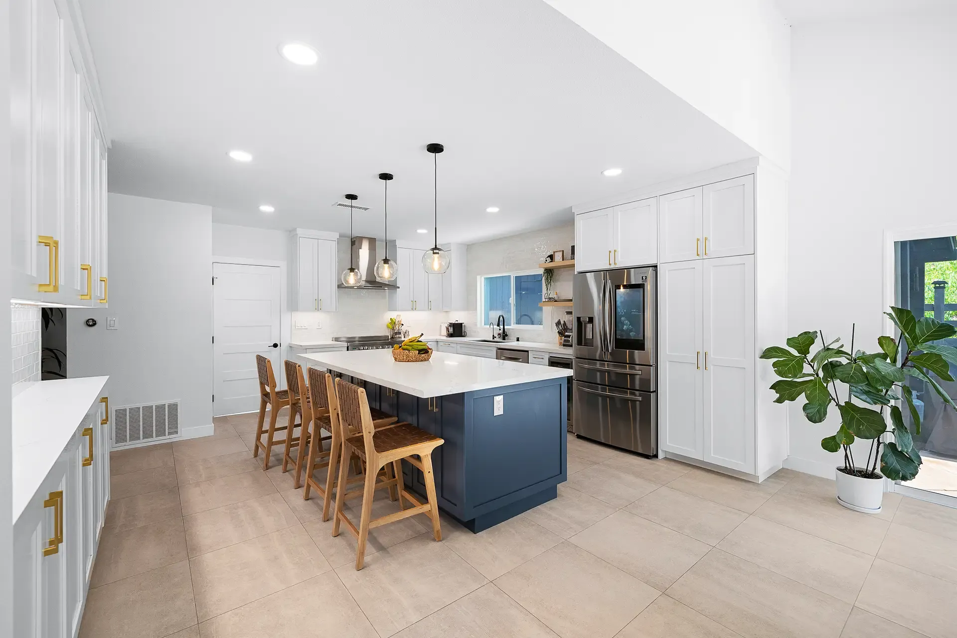 Open kitchen with navy island, wood barstools, pendants and white cabinetry