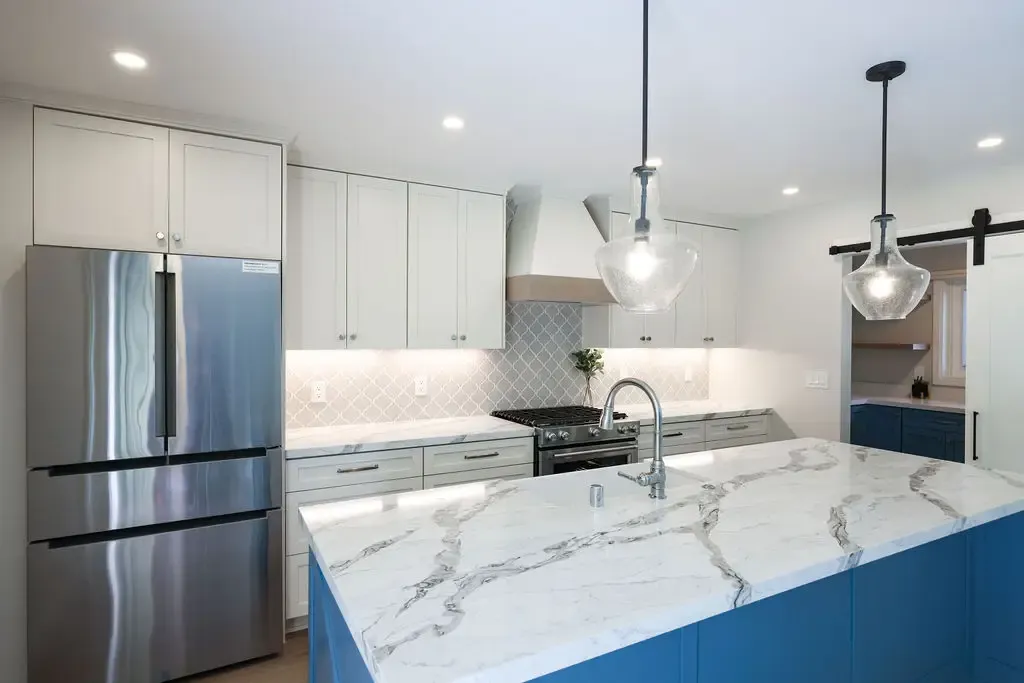 Open kitchen with white marble waterfall island, blue base, and arabesque tile backsplash