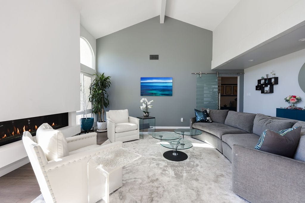 Open living room with linear fireplace, curved gray sectional and glass tables