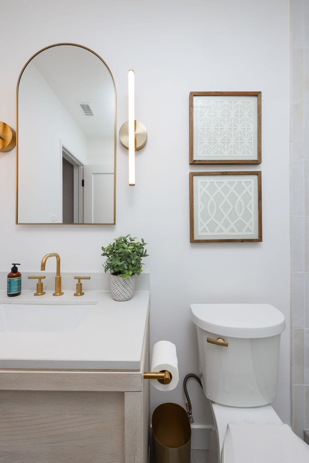 powder bath with arched gold mirror, oak vanity and framed wall art