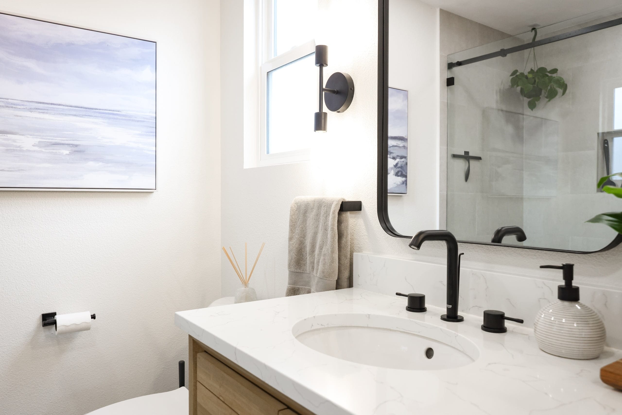 Powder bath with oak vanity, marble counter, coastal art and black mirror