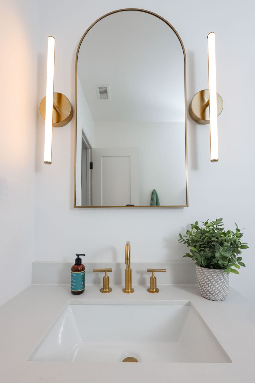 powder room vanity with brass widespread faucet, arched mirror and linear gold sconces