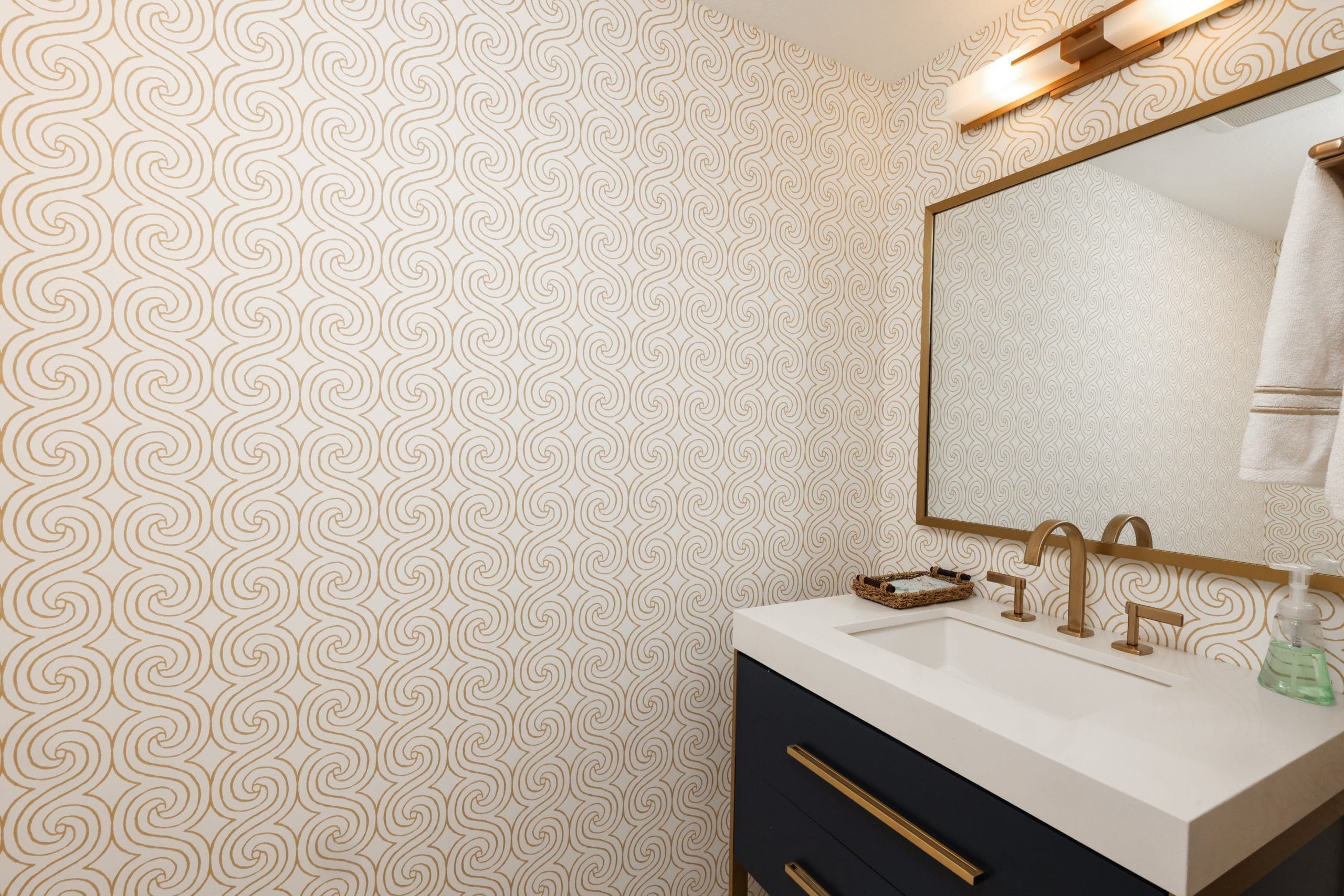 Powder room with gold swirl wallpaper, navy vanity and brass faucet