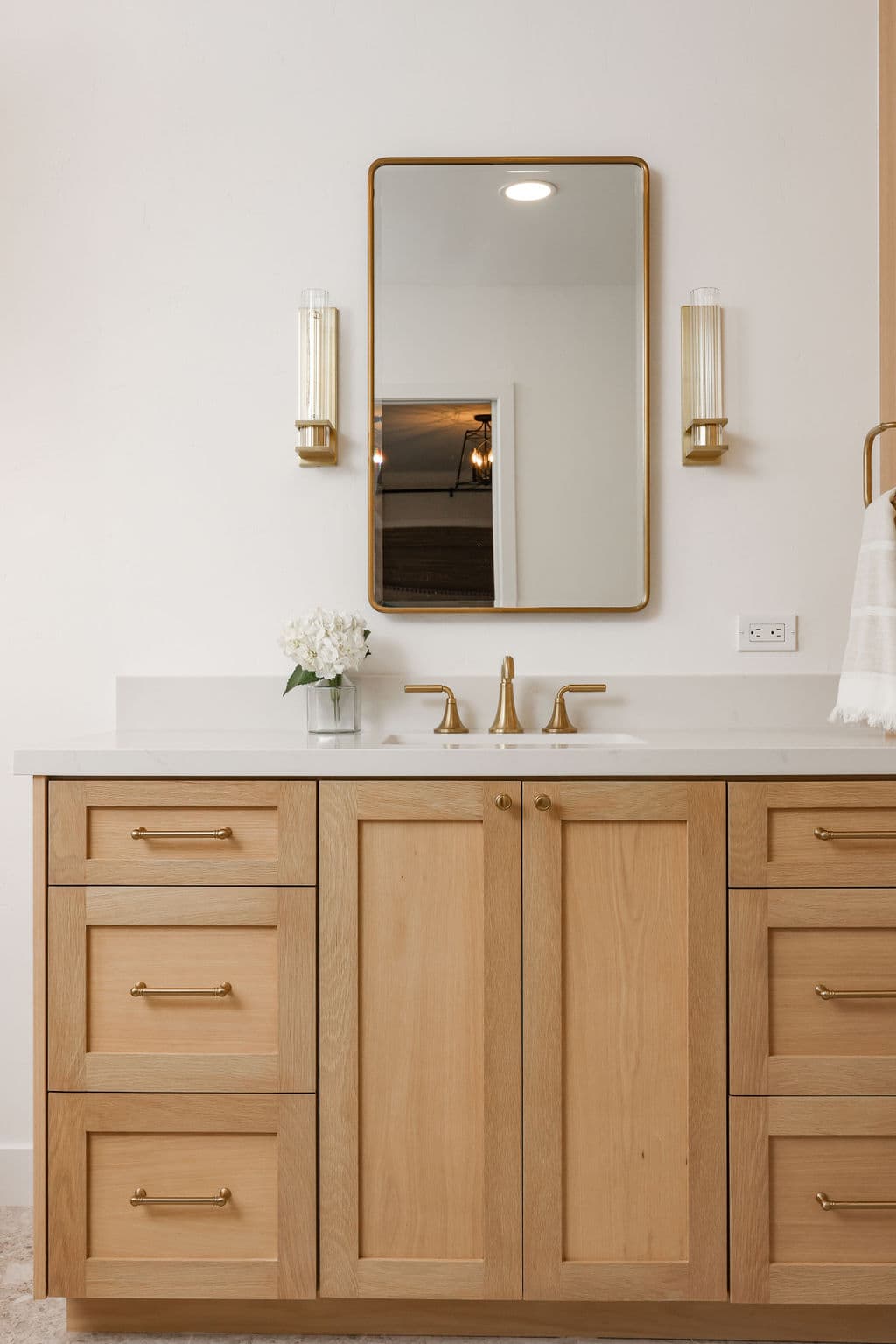 Primary bath vanity in white oak with brass sconces and arched framed mirror