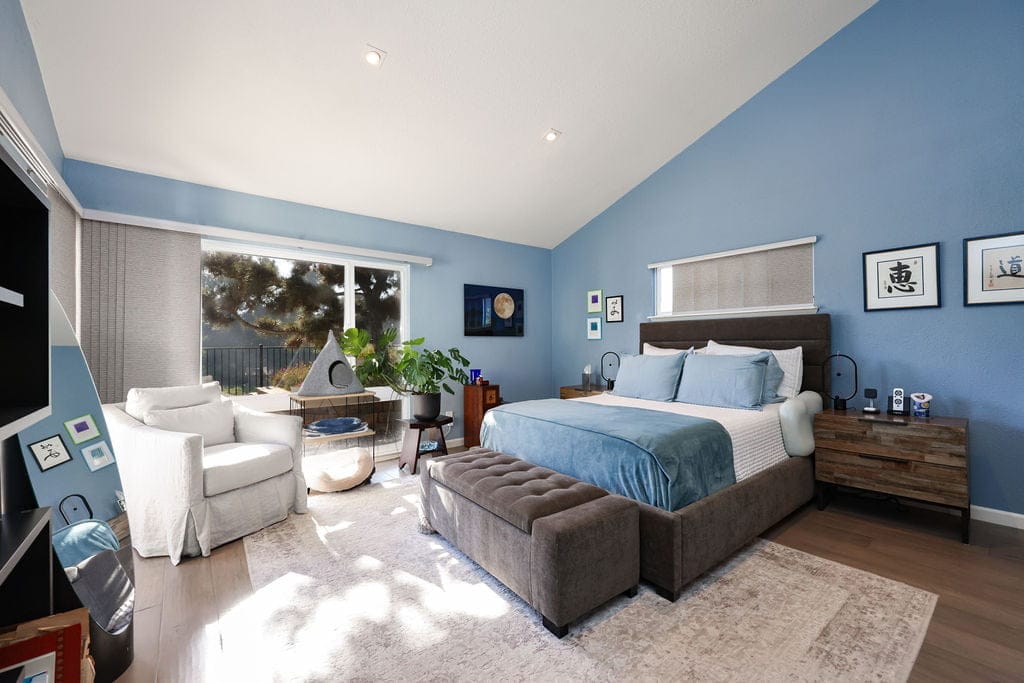 Primary bedroom with blue accent wall, upholstered bed, vaulted ceiling, and oak flooring